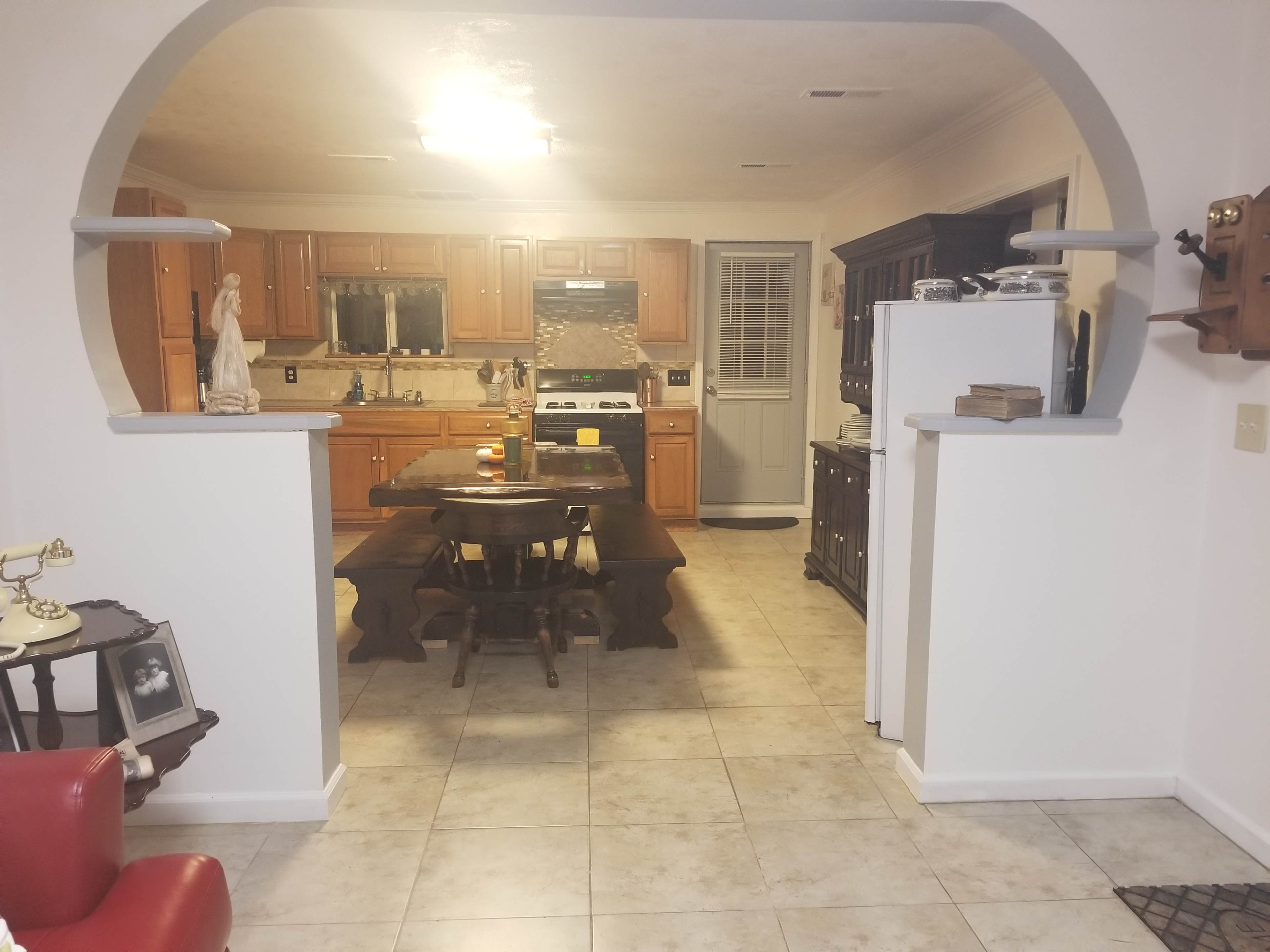 A spacious kitchen with wooden cabinets, a large dining table in the center, and a doorway leading to a side entrance.