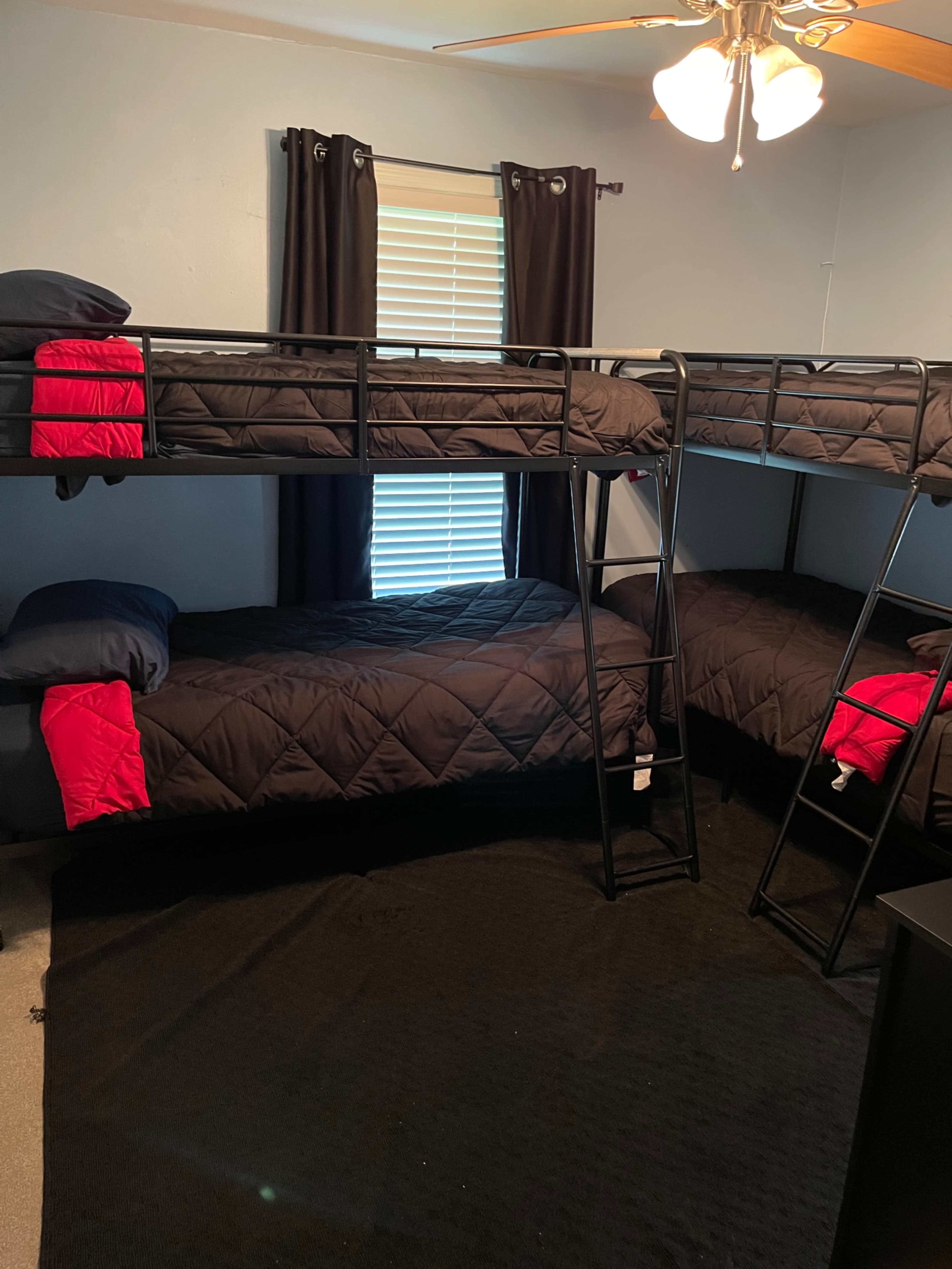 A bedroom with a black metal bunk bed, featuring two sets of twin-sized beds with dark bedding and a black carpet.