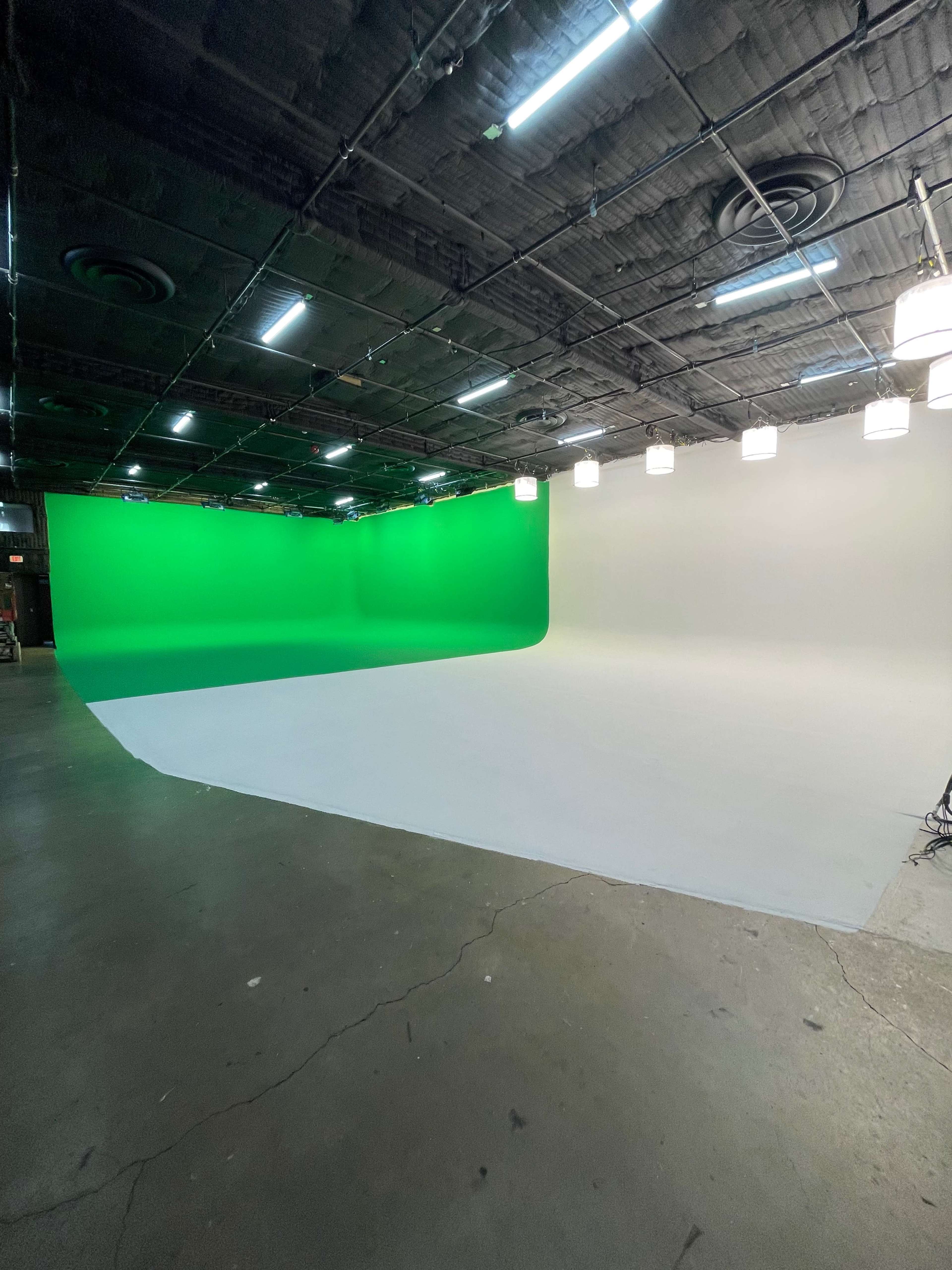 A large studio space with a green screen on one side and a gray background on the opposite side, illuminated by overhead lights.