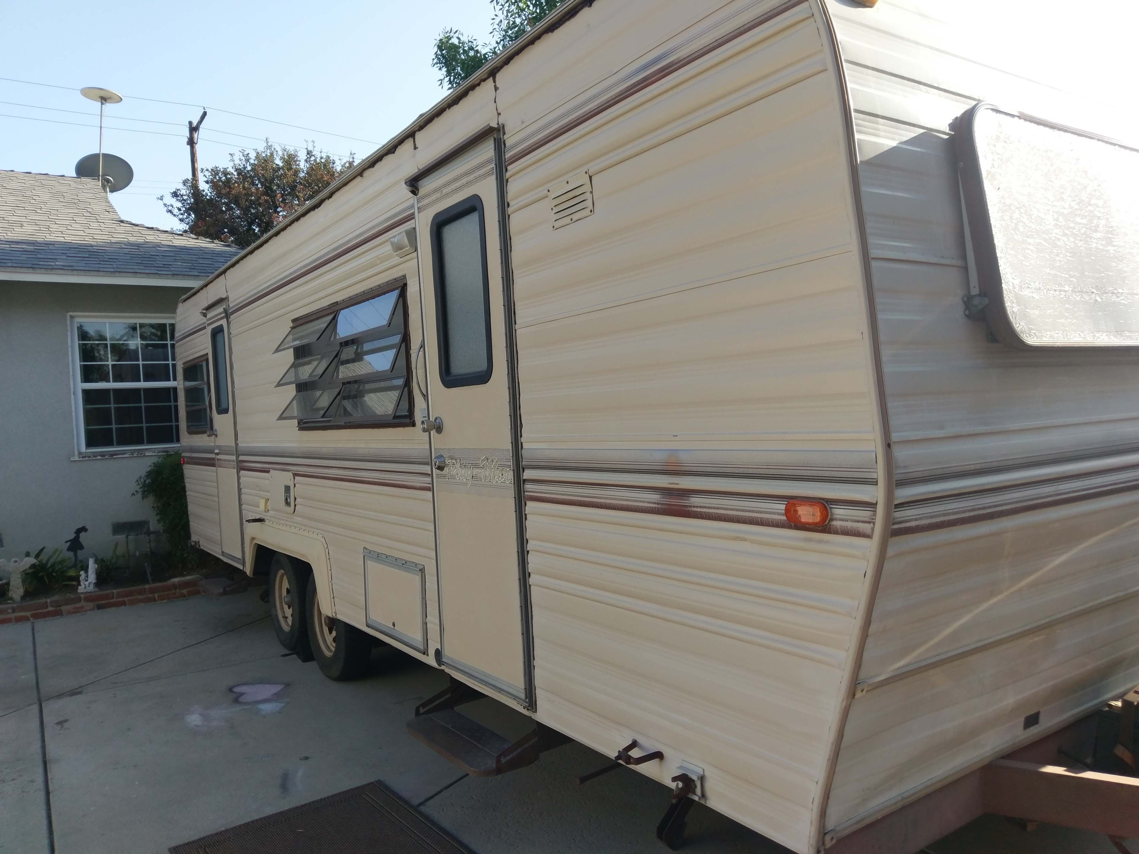 A vintage camper trailer is parked on a driveway beside a house.