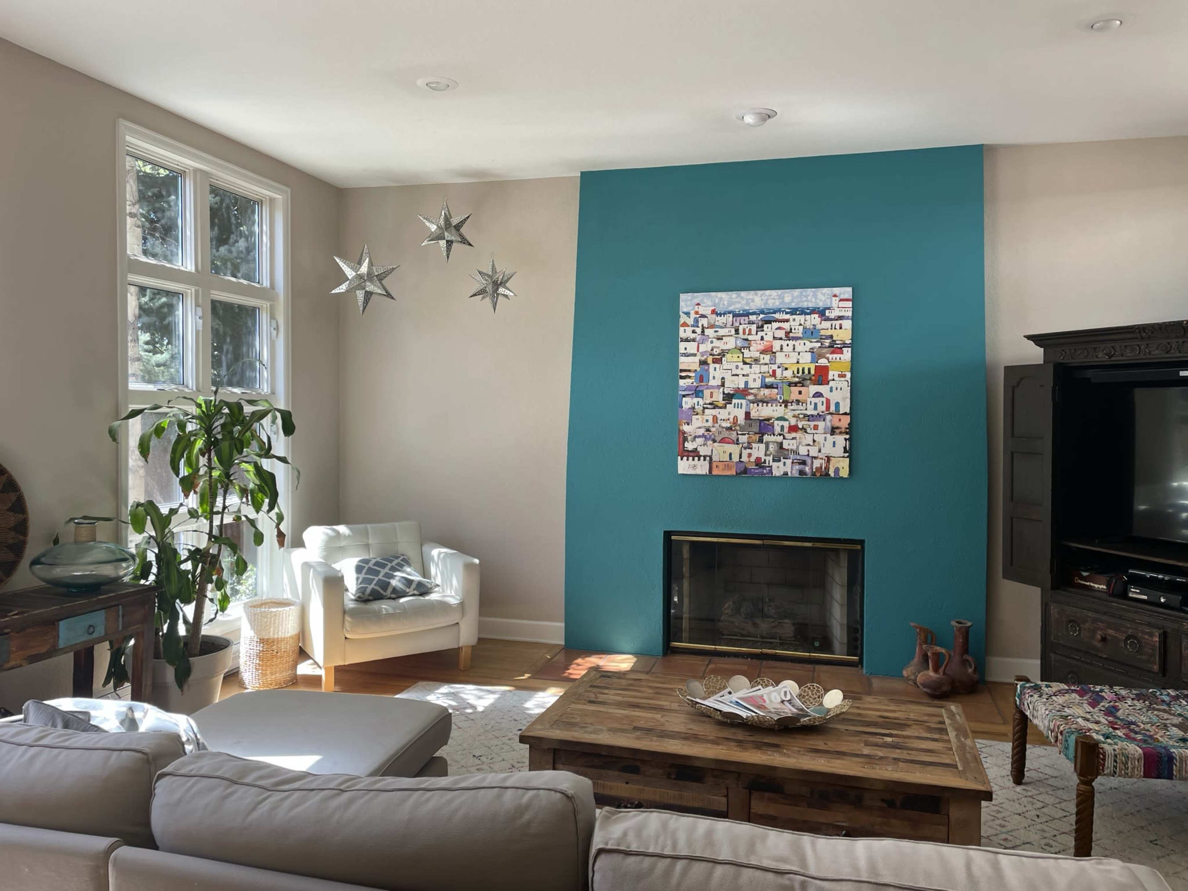 A living room features a turquoise accent wall, a fireplace, a coffee table, and a large piece of colorful artwork.
