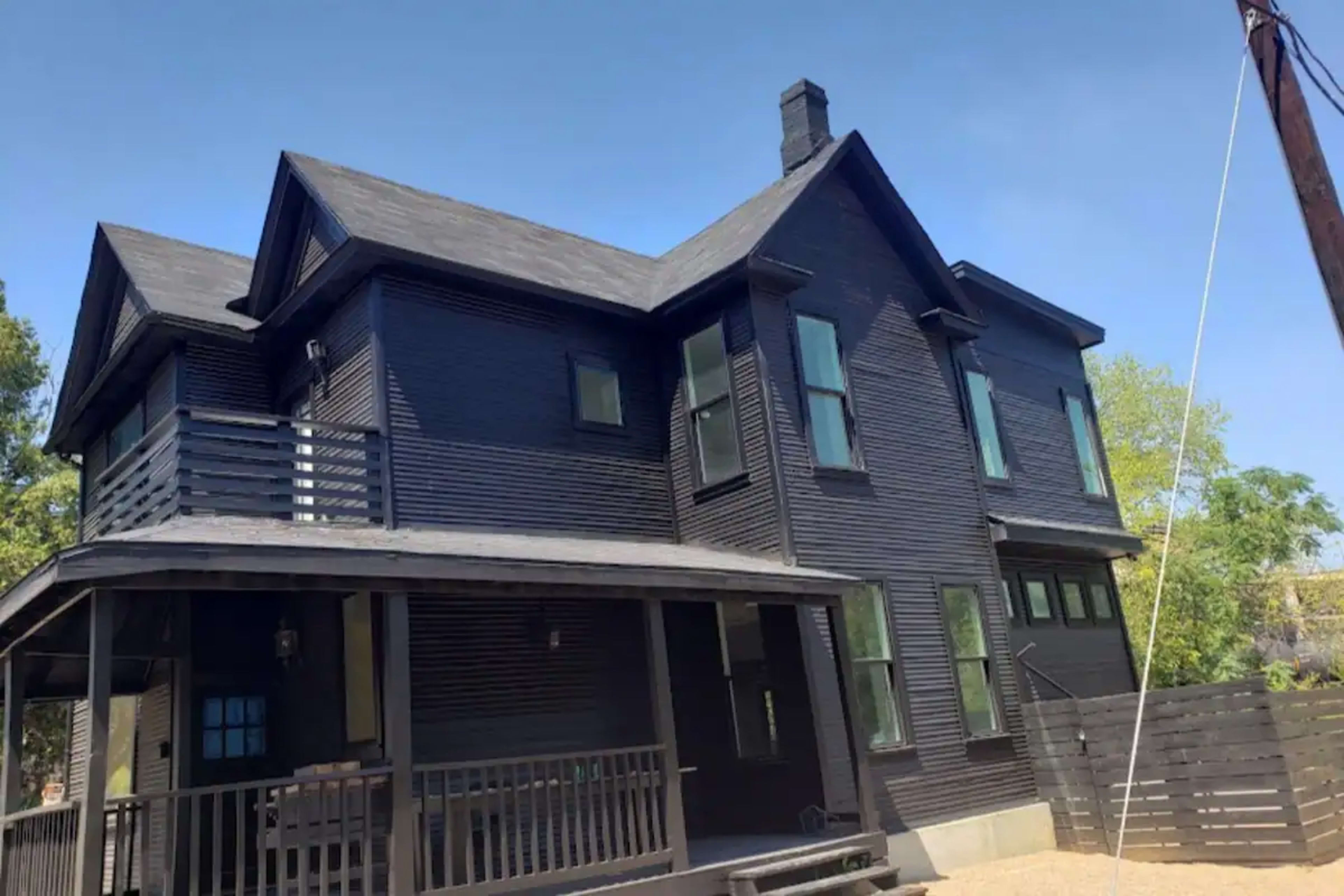A two-story black house with multiple windows and a front porch, set against a clear blue sky.
