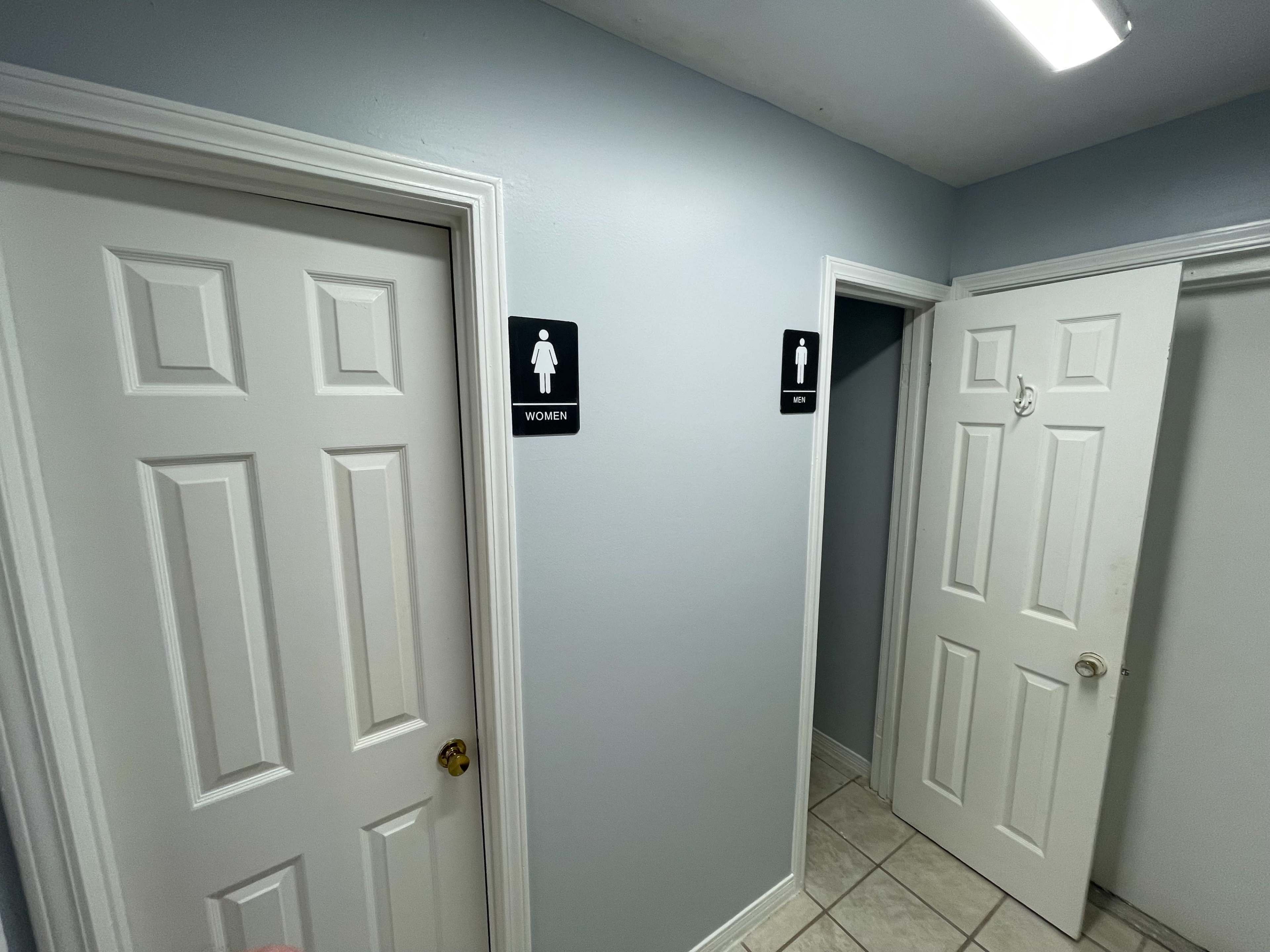 The image shows two doors in a hallway, one labeled "WOMEN" and the other partially open, leading to a bathroom area.