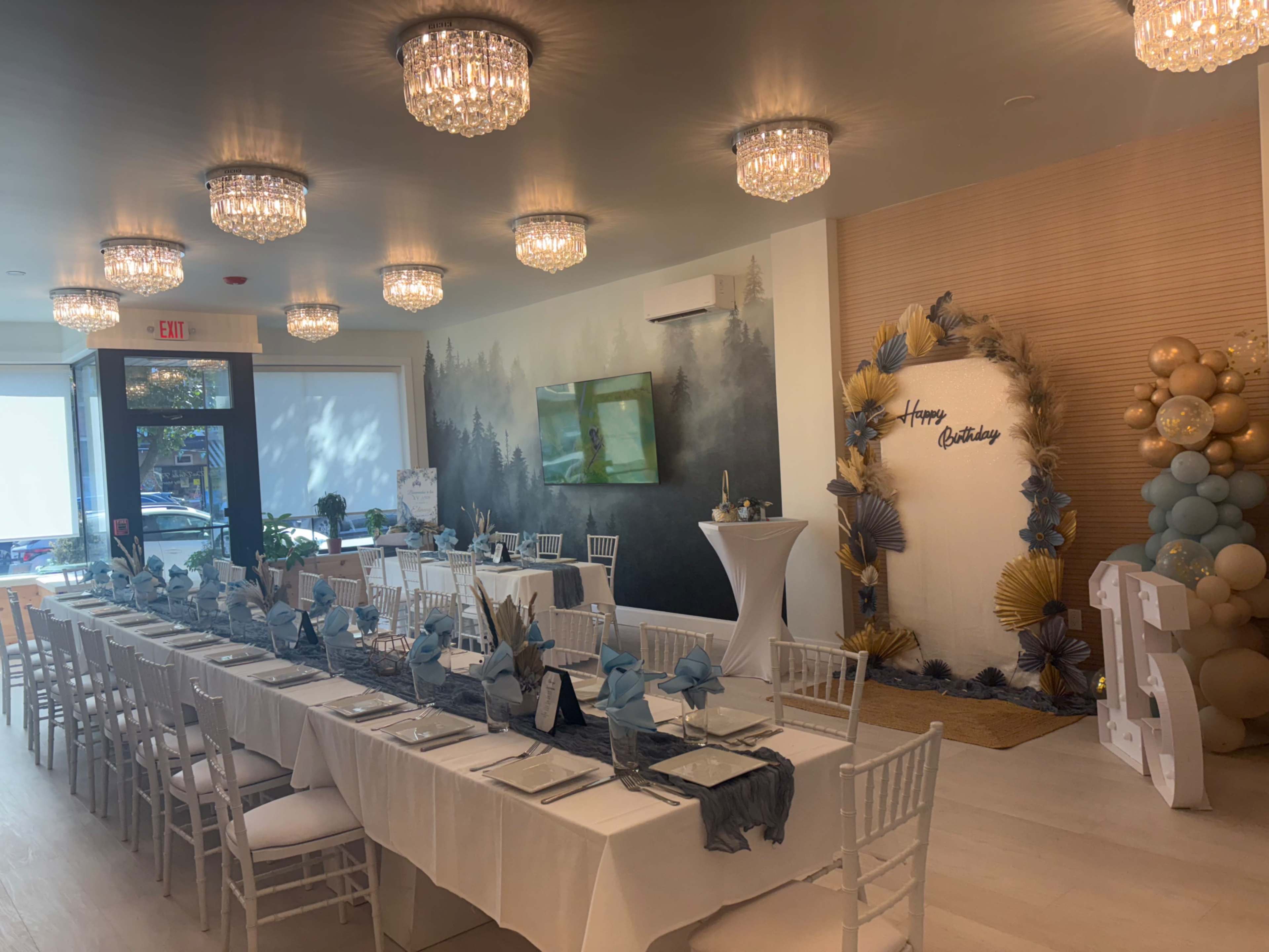 The image shows a well-decorated dining area for a birthday celebration, featuring a long table set with tableware and a decorative backdrop with balloons and a "Happy Birthday" sign.