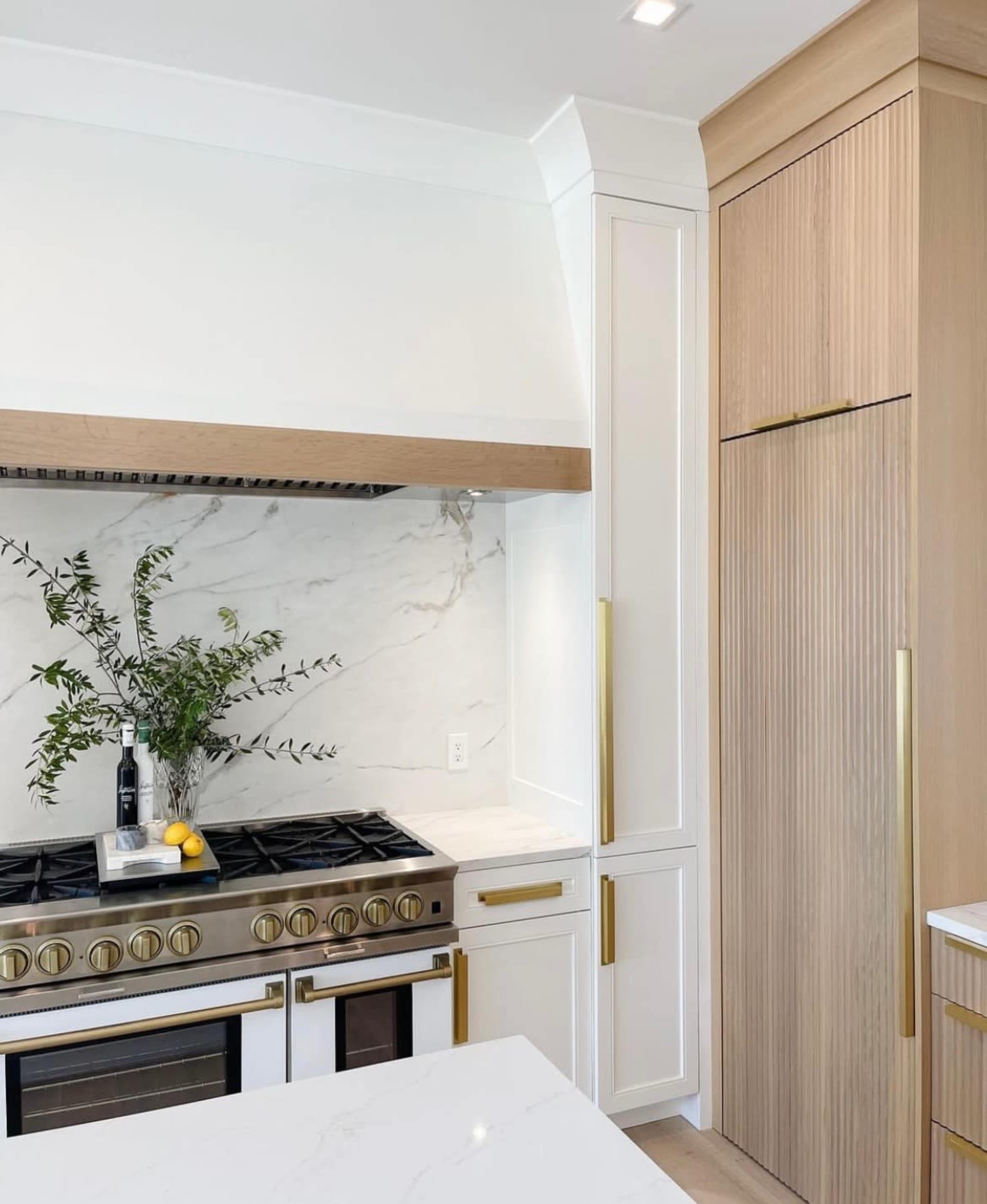 The image shows a modern kitchen with a stainless steel stove, a marble backsplash, and cabinetry featuring wood accents.