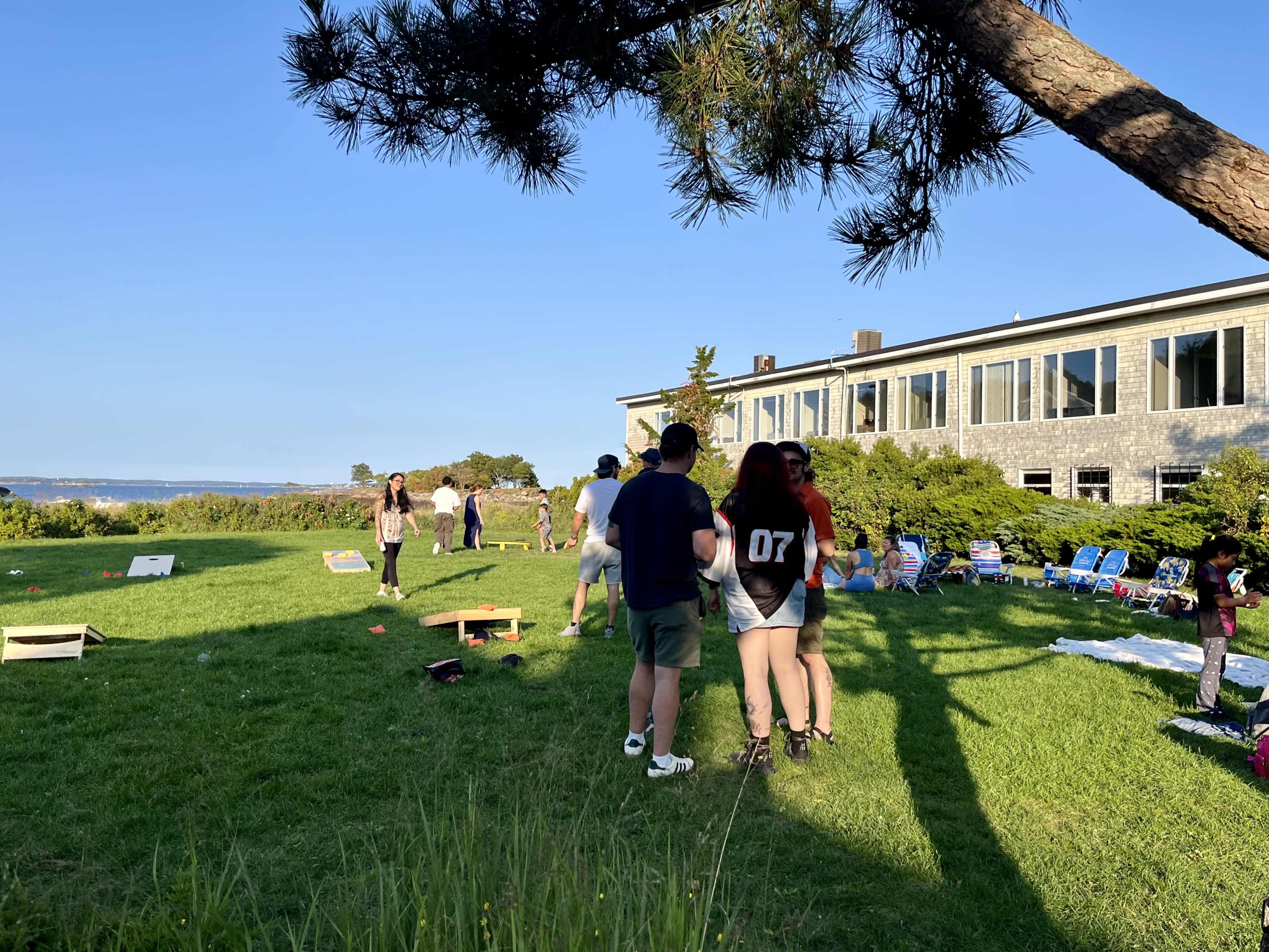 People are gathered on a grassy area near a building, engaging in various activities while enjoying the outdoors.