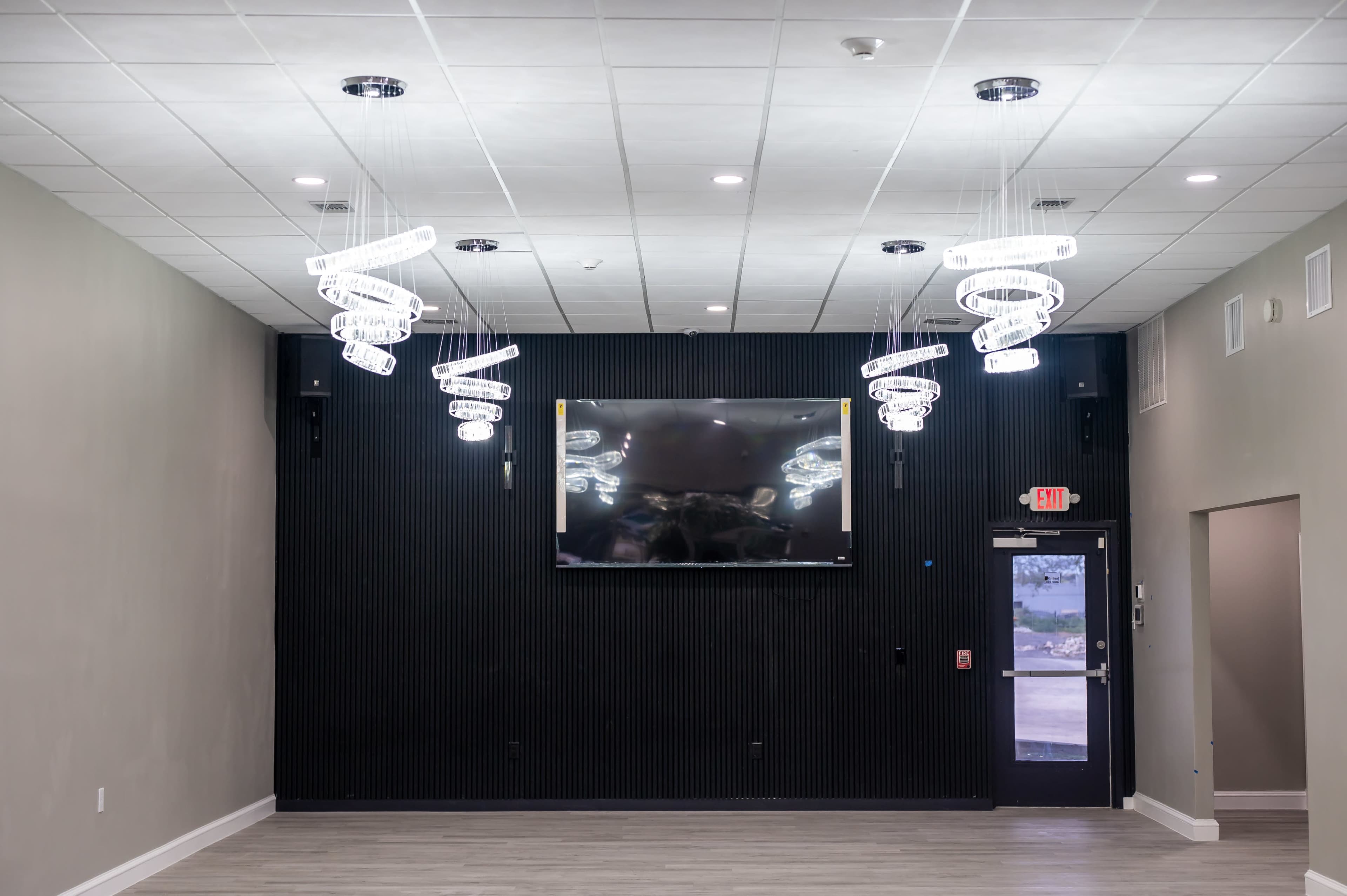 The image shows a modern interior space with a large wall-mounted television, illuminated by spiral pendant lights, and a door leading outside.
