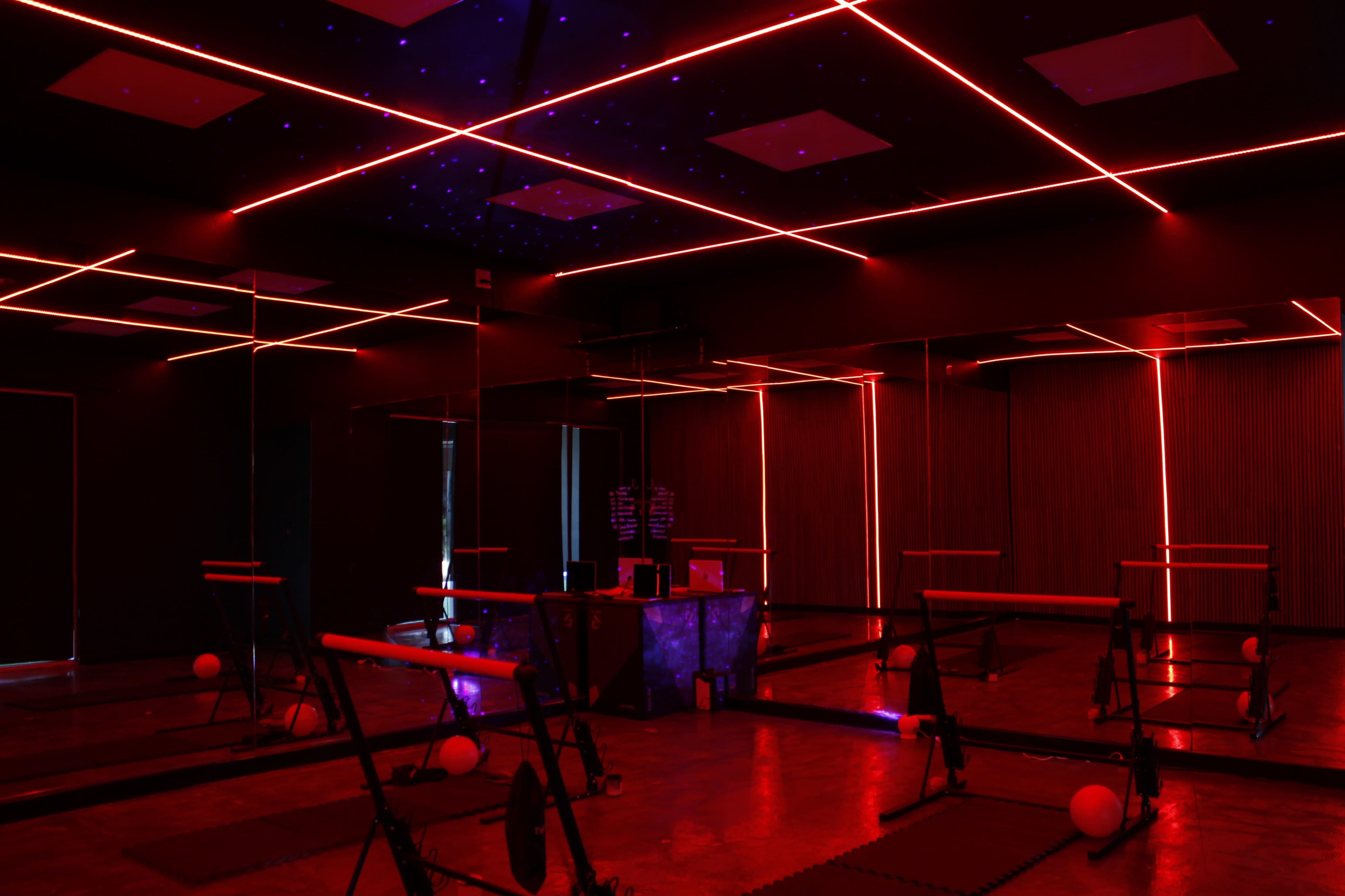 A dimly lit fitness studio featuring red neon lights, mirrors, and exercise equipment arranged in rows.