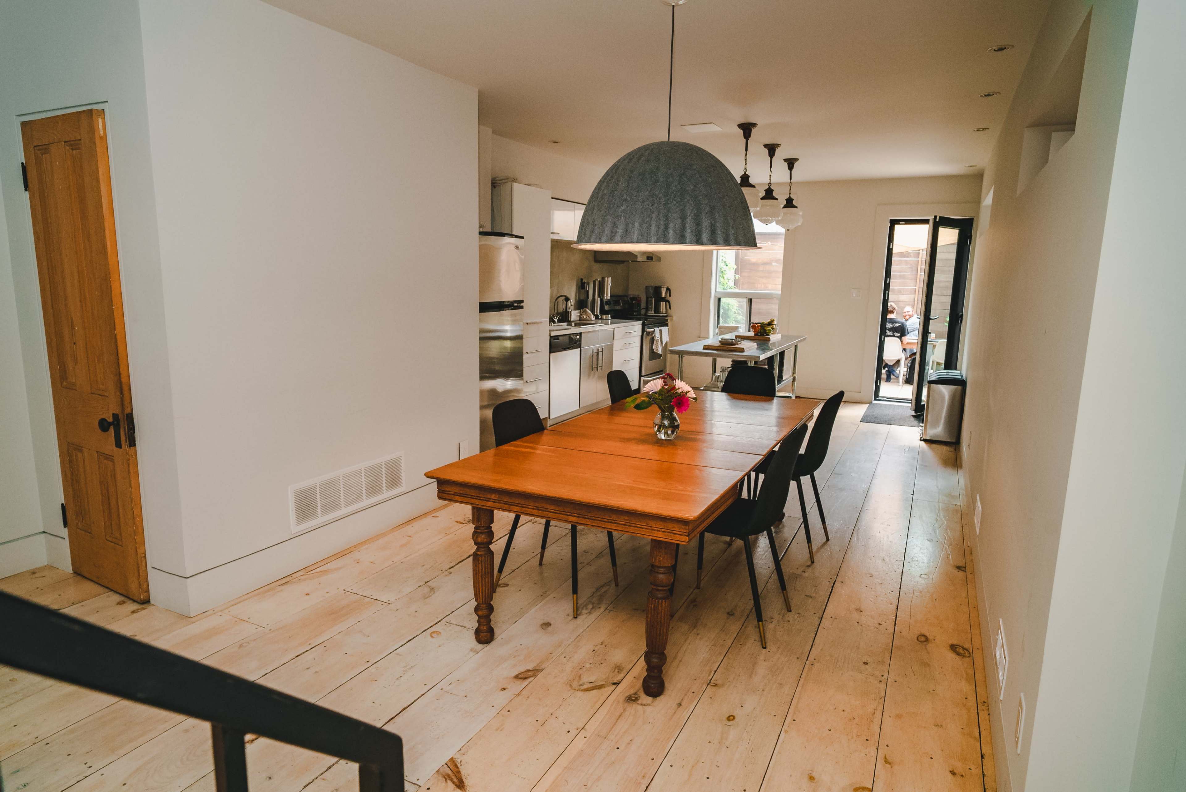 A spacious dining area features a wooden table surrounded by black chairs, with a well-equipped kitchen visible in the background.