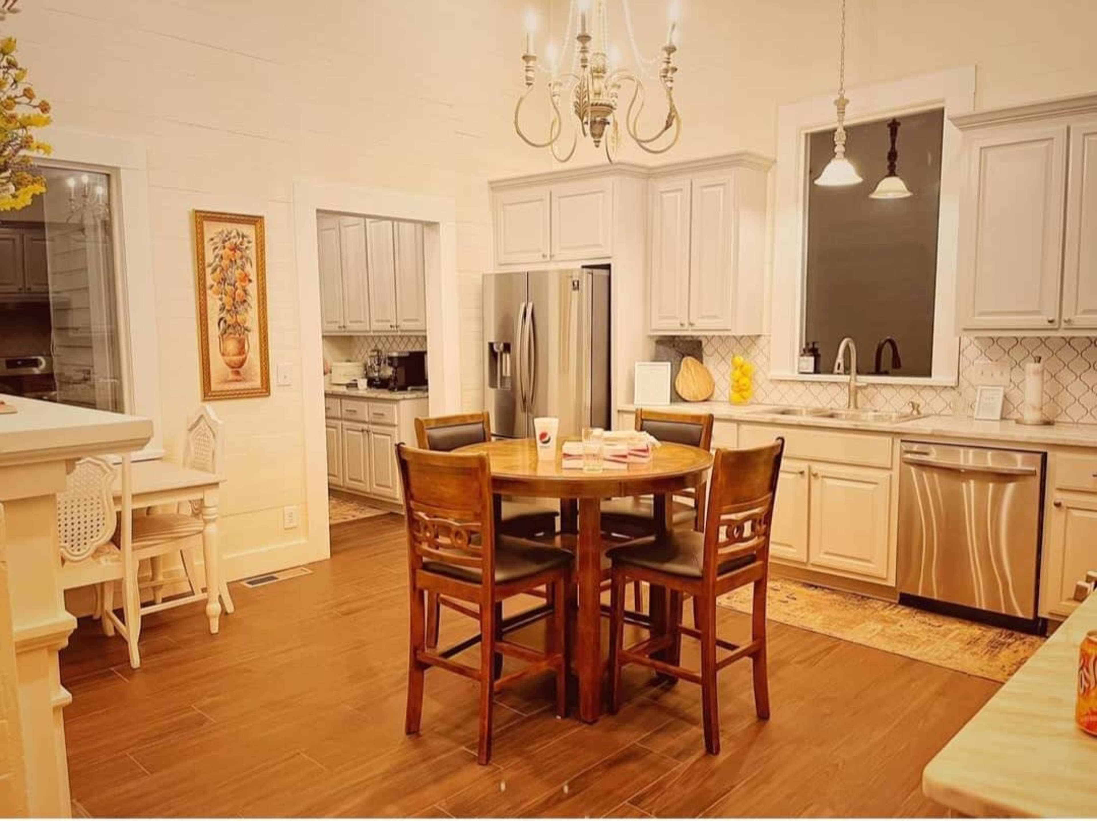 A modern kitchen featuring gray cabinets, stainless steel appliances, a round wooden dining table with four chairs, and a chandelier above.