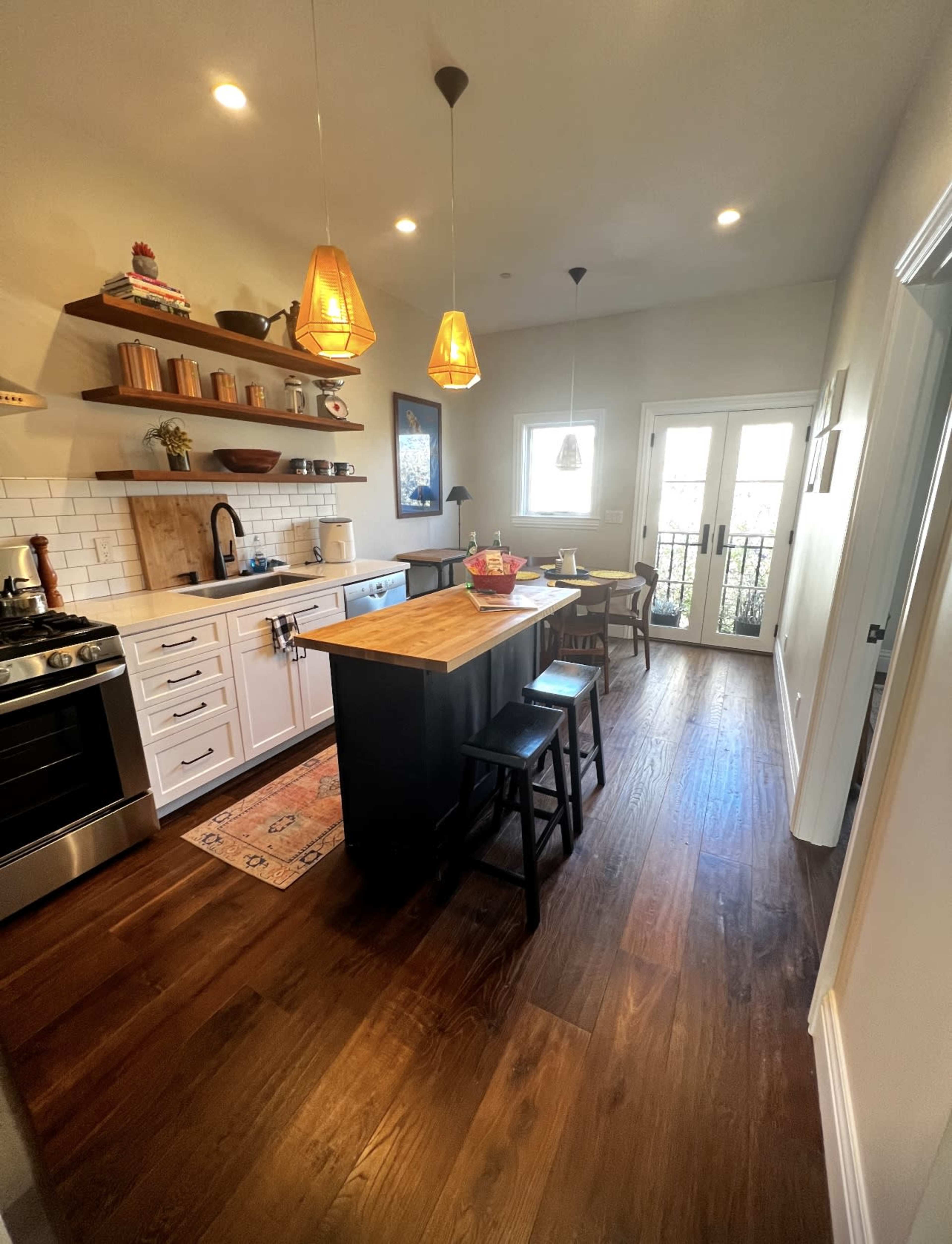 The kitchen features a central island with seating, open shelves displaying kitchenware, and a mix of modern and classic design elements.