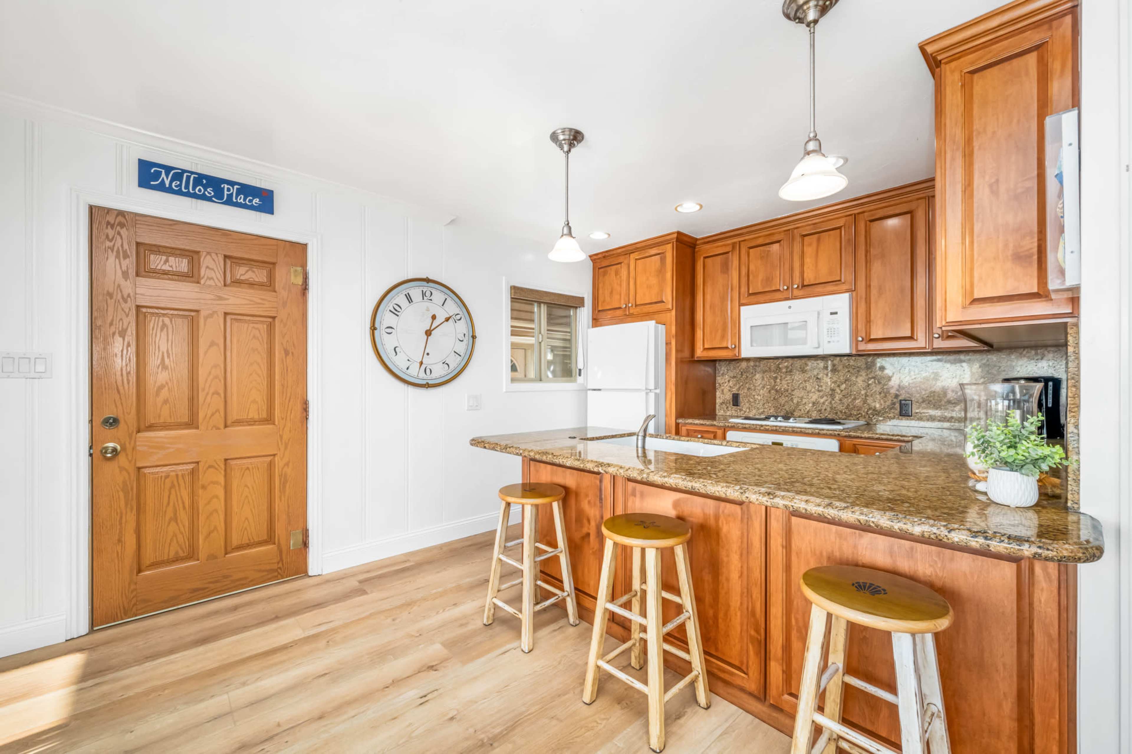 A kitchen with wooden cabinetry, a countertop seating area with three stools, and a door labeled "Hello's Place."
