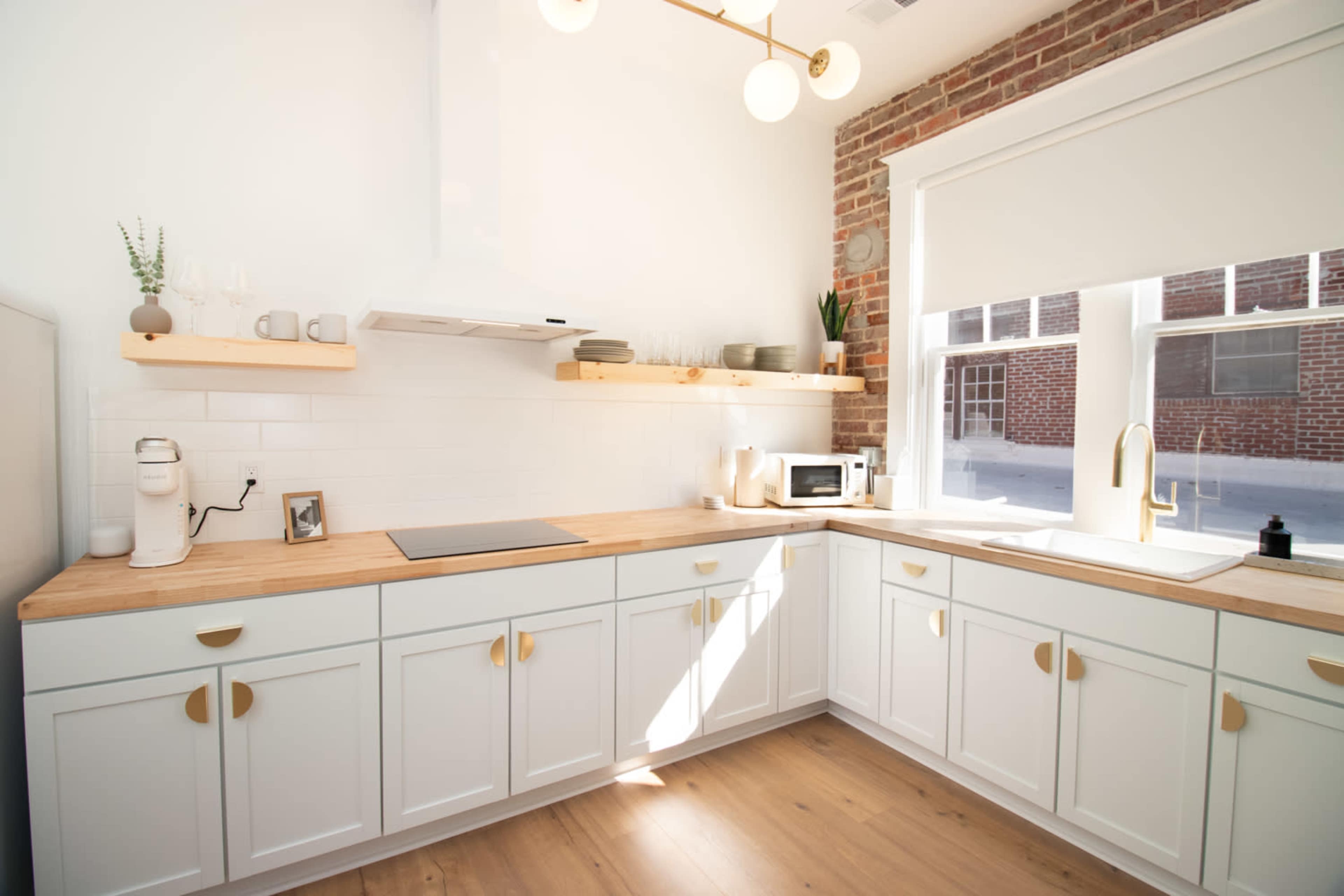 A modern kitchen with white cabinetry, a wooden countertop, a sink, and a window that provides natural light.