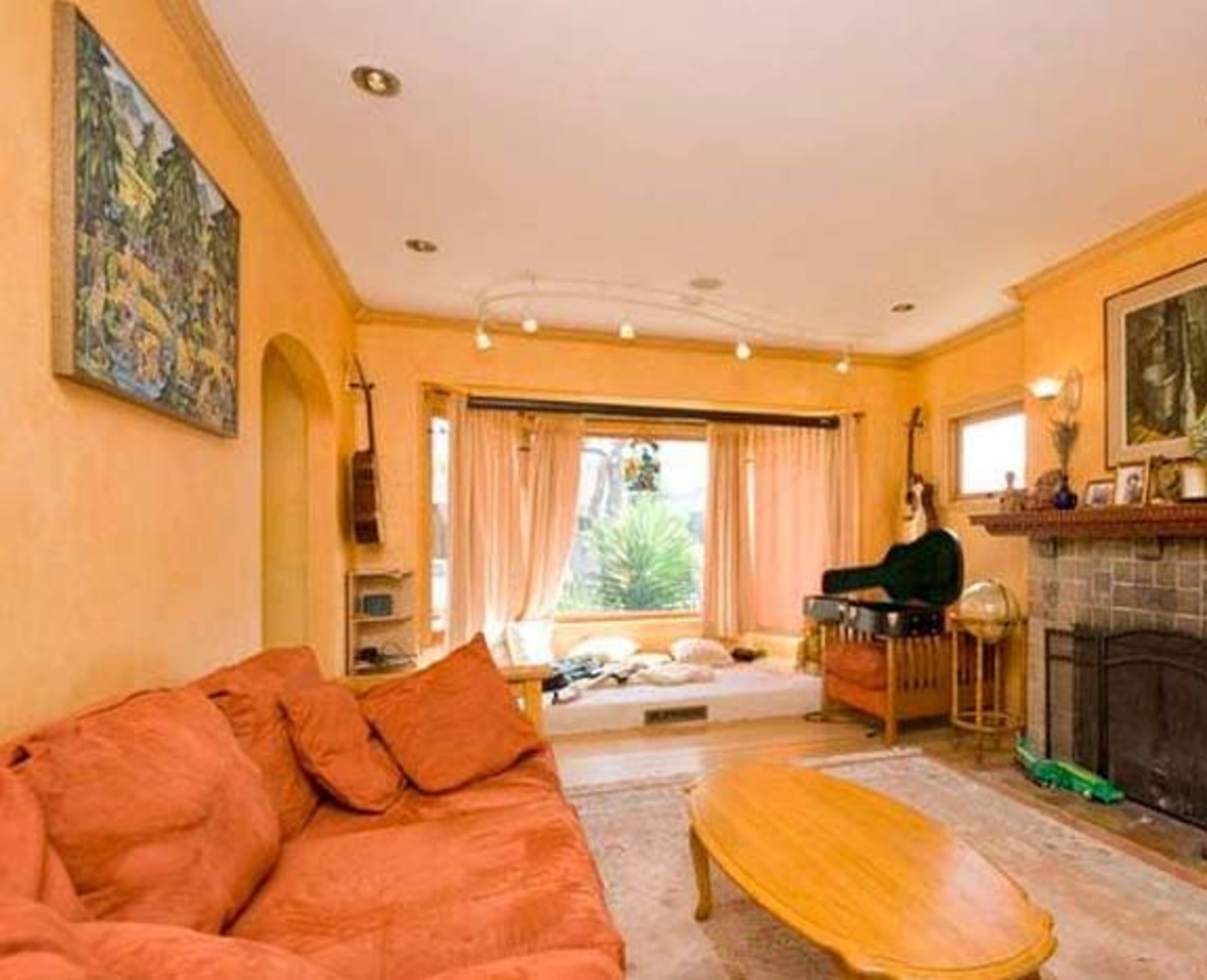 A living room with orange walls, a large sectional sofa, and a bay window overlooking greenery.