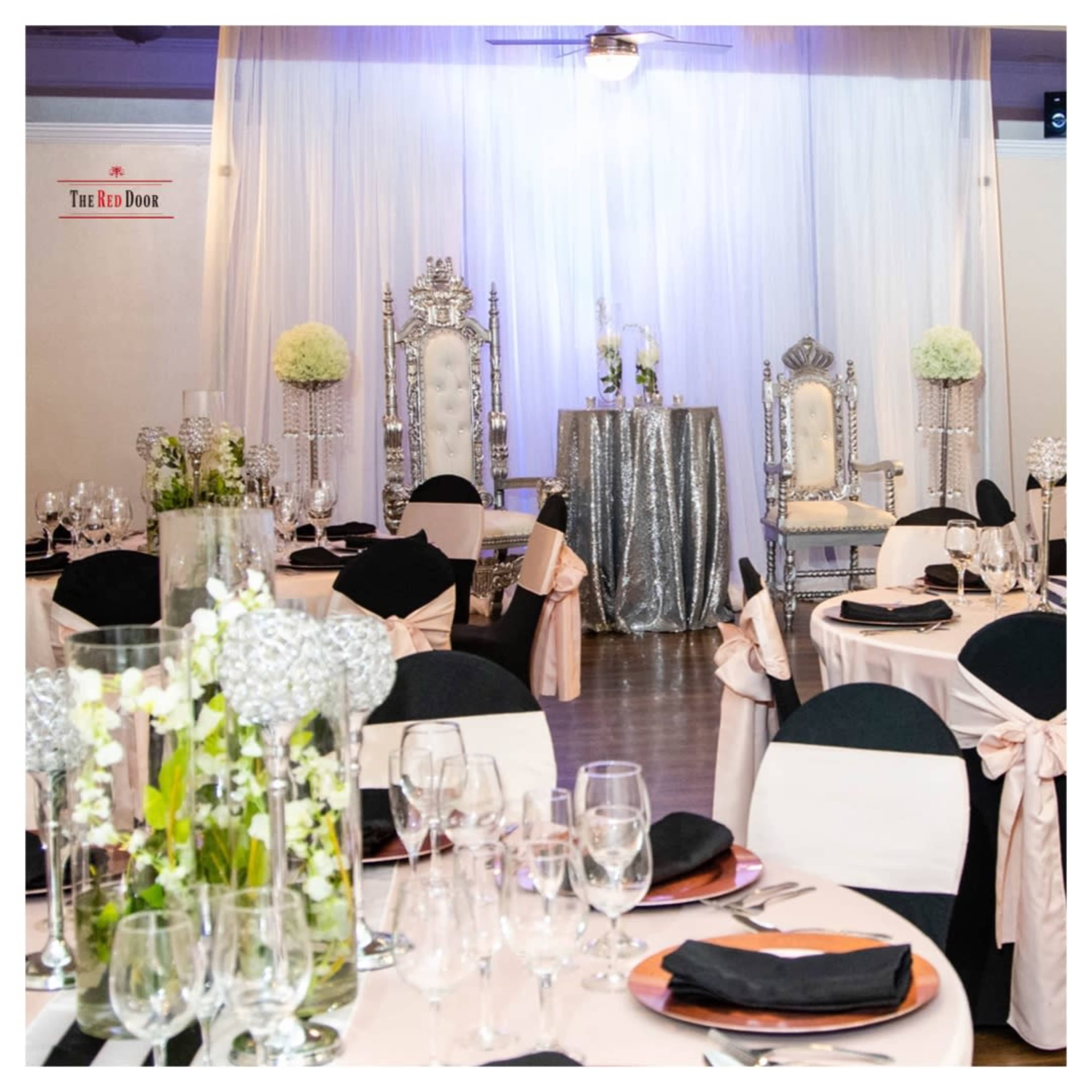 The elegant event space features round tables adorned with black and peach tablecloths, crystal glassware, and two ornate throne-like chairs against a backdrop of flowing white drapes.