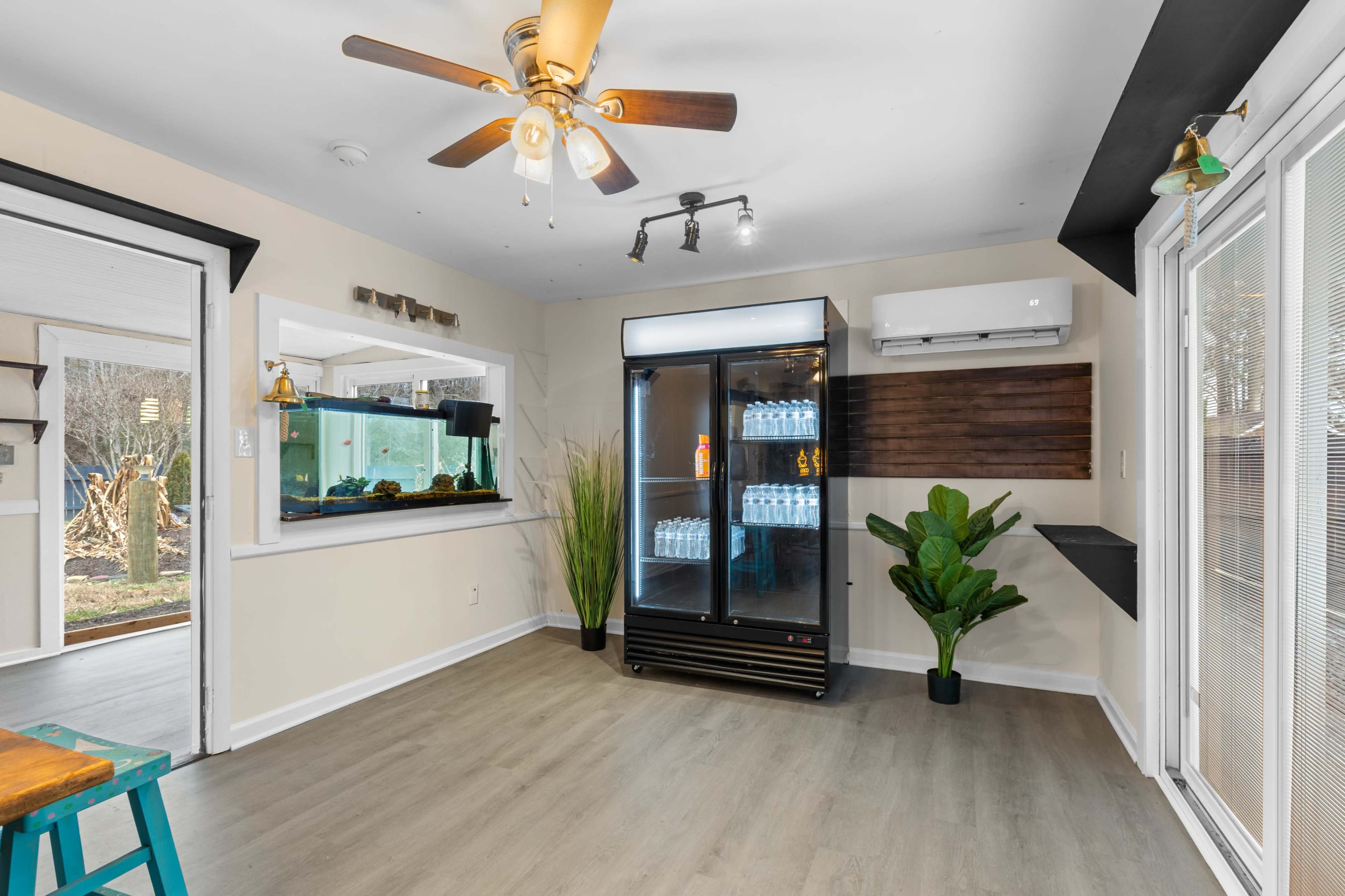The room features a ceiling fan, a large glass refrigerator, an aquarium, and a potted plant in a corner with light-colored flooring.