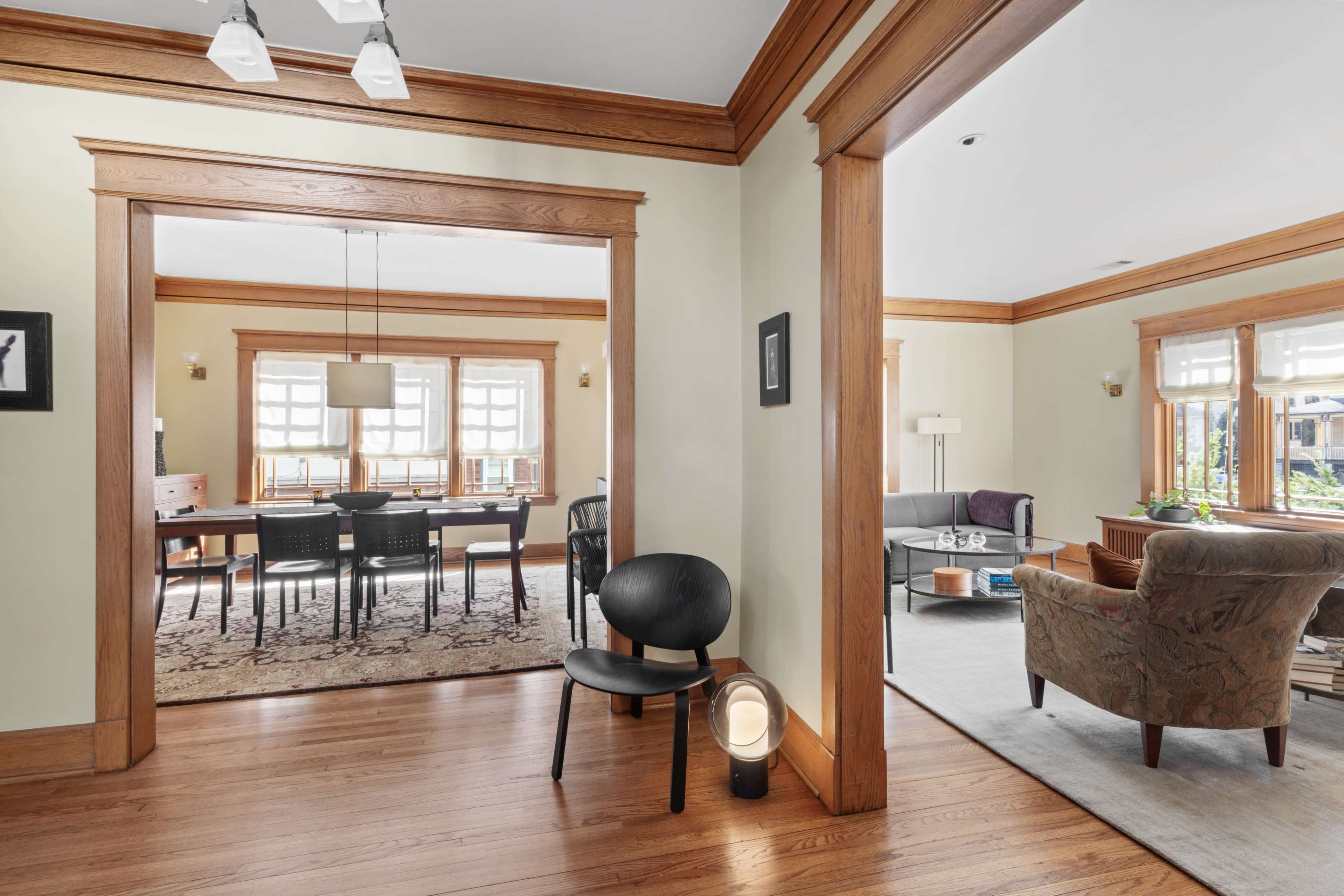 The image shows an interior space featuring an open living area connected to a dining room, with wooden trim and furniture arranged for seating.