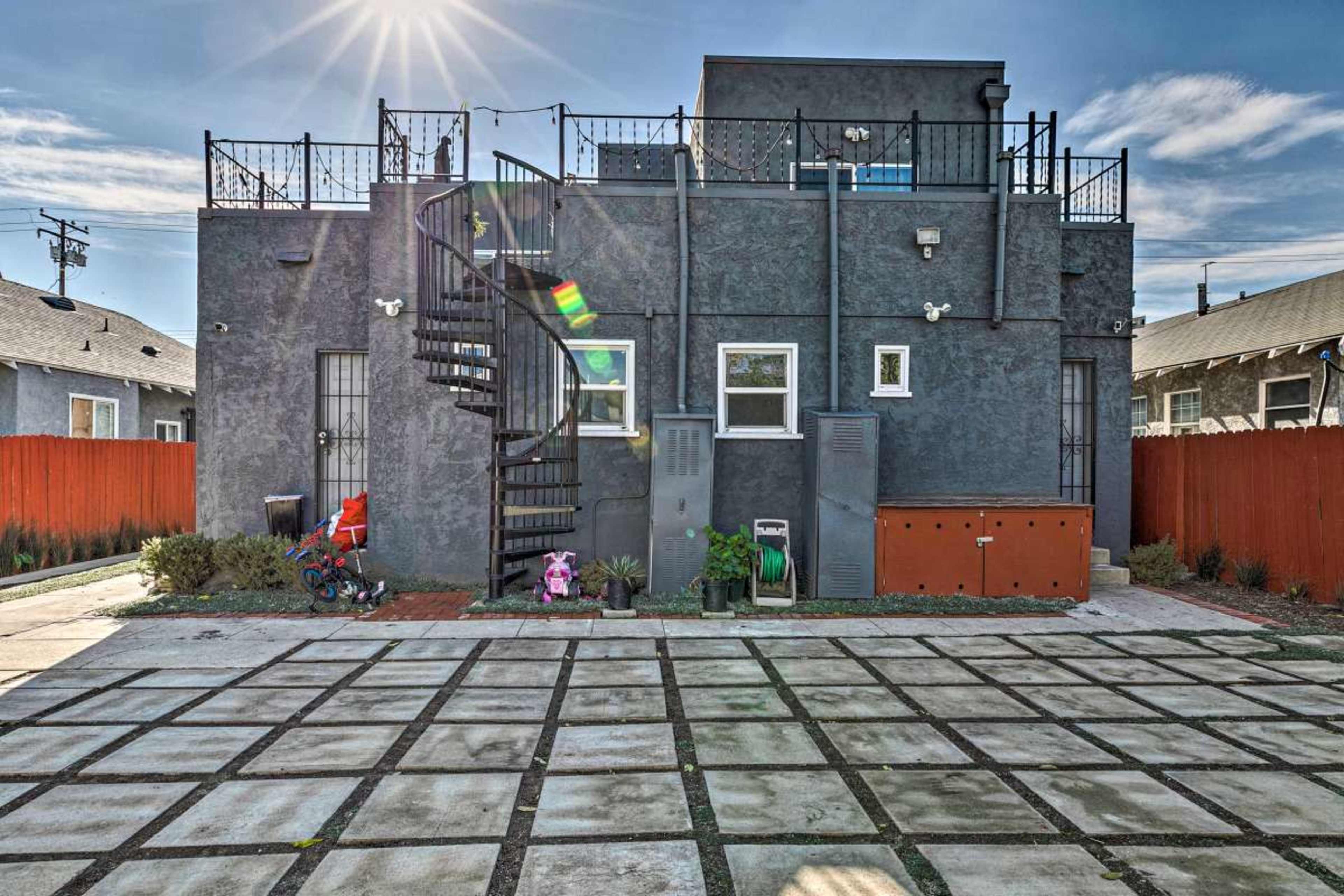 The image shows a two-story gray building with a spiral staircase, surrounded by a fenced yard and a paved ground area.