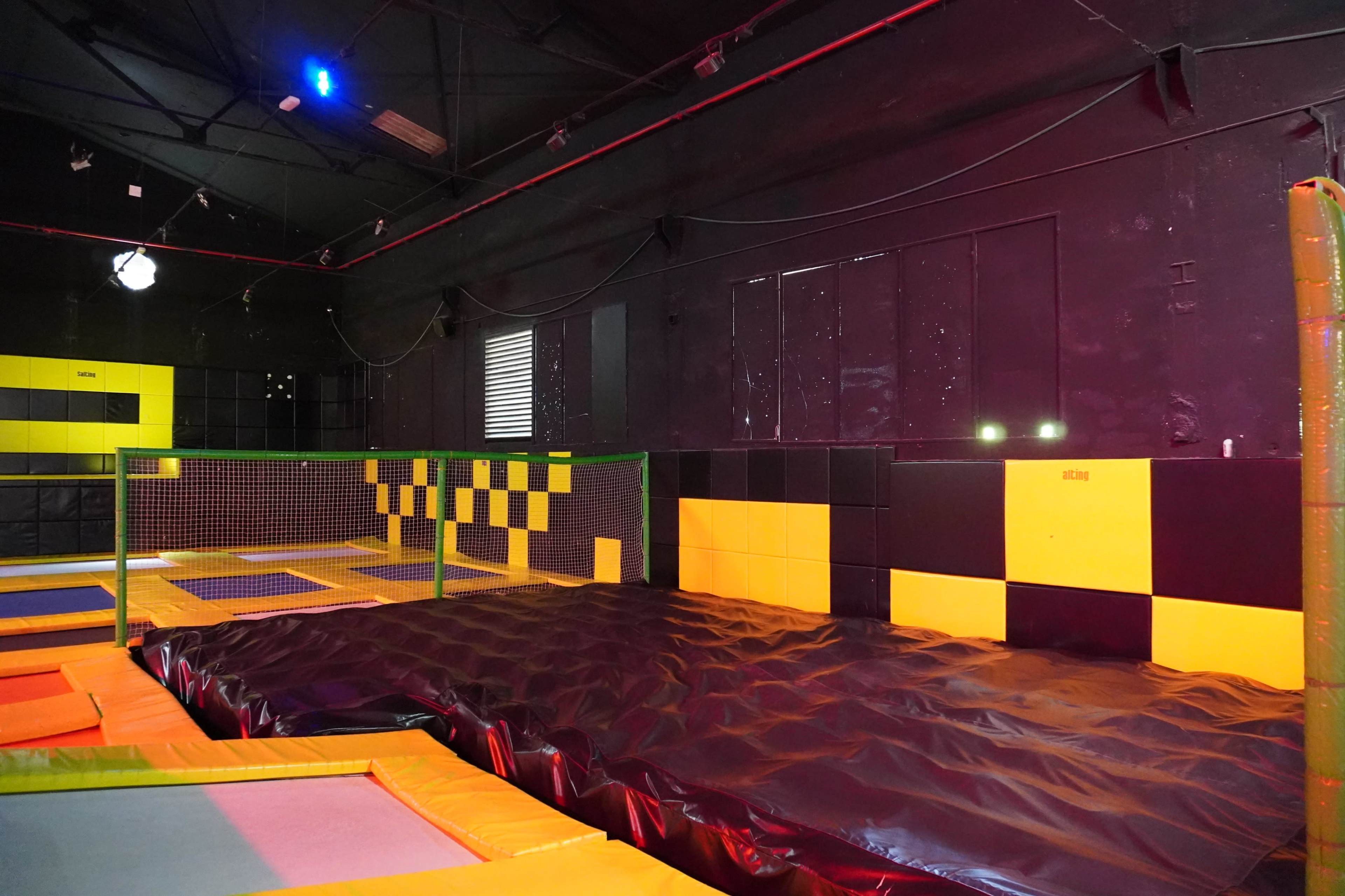 An indoor trampoline park featuring an arrangement of colorful trampolines, a padded area for jumping, and black and yellow wall decorations.