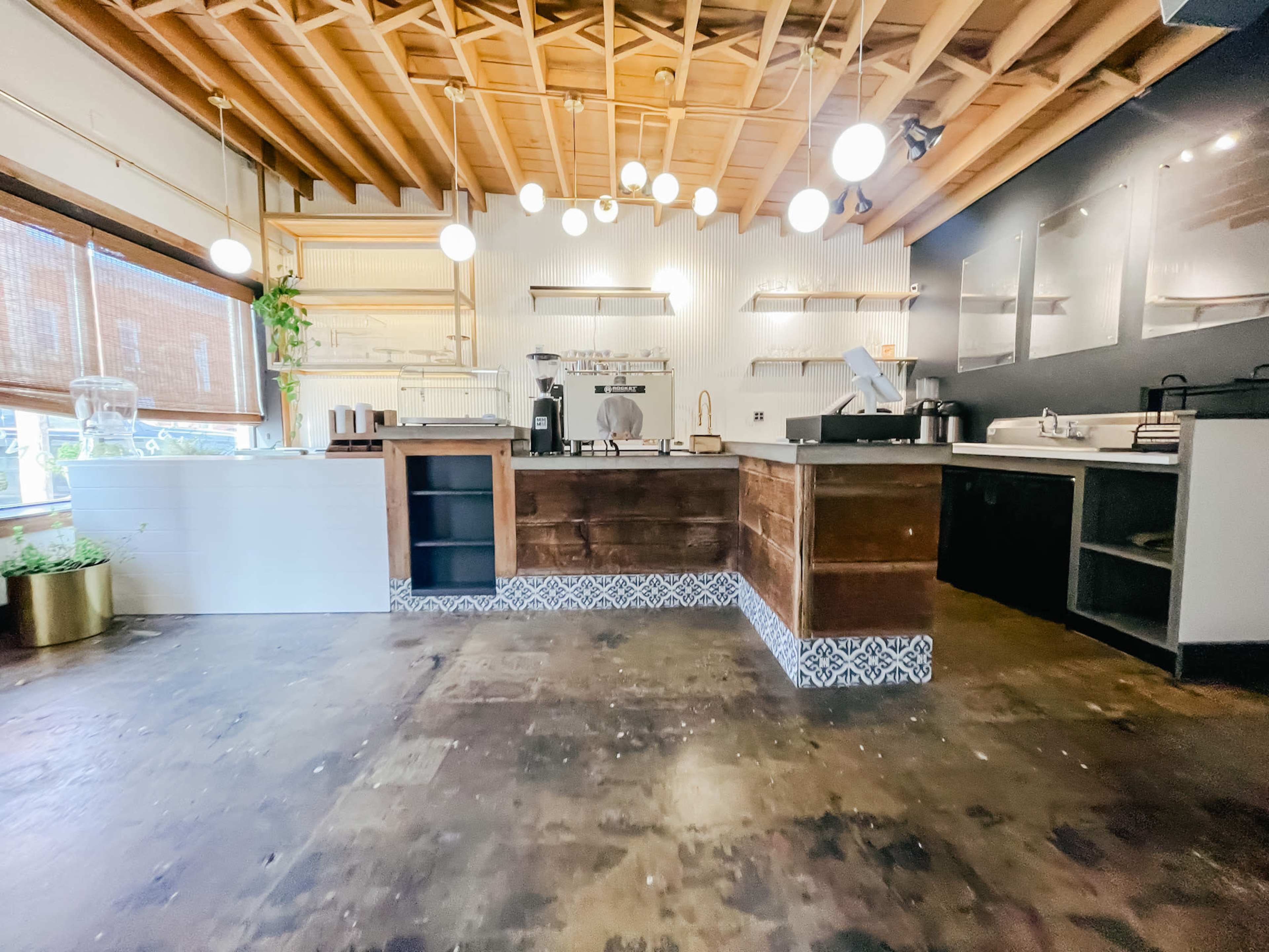 A modern café interior with wooden cabinetry, pendant lighting, and a polished floor featuring a patterned tile border.
