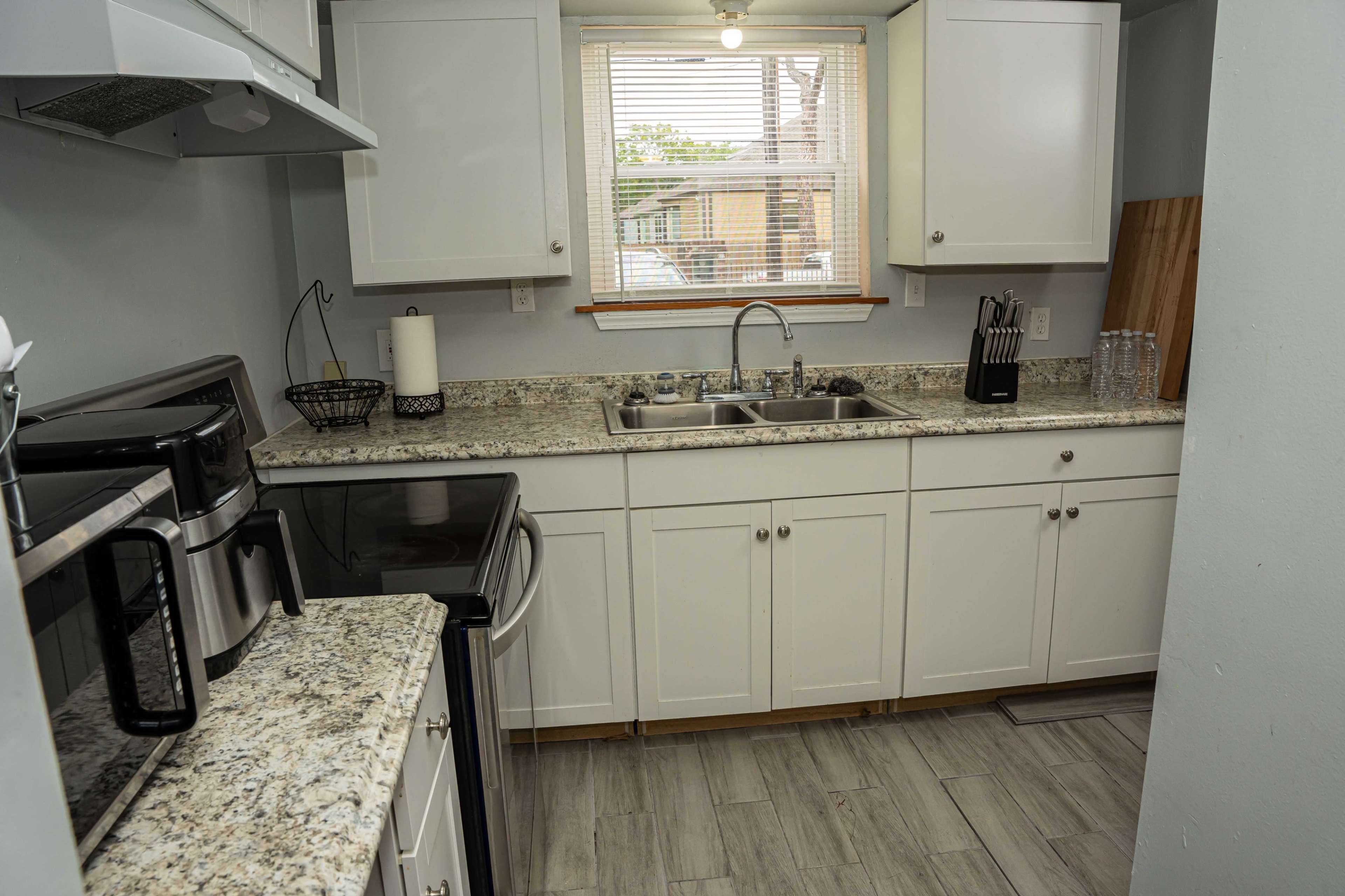A modern kitchen with granite countertops, white cabinets, a double sink, and various appliances including a coffee maker and an oven.