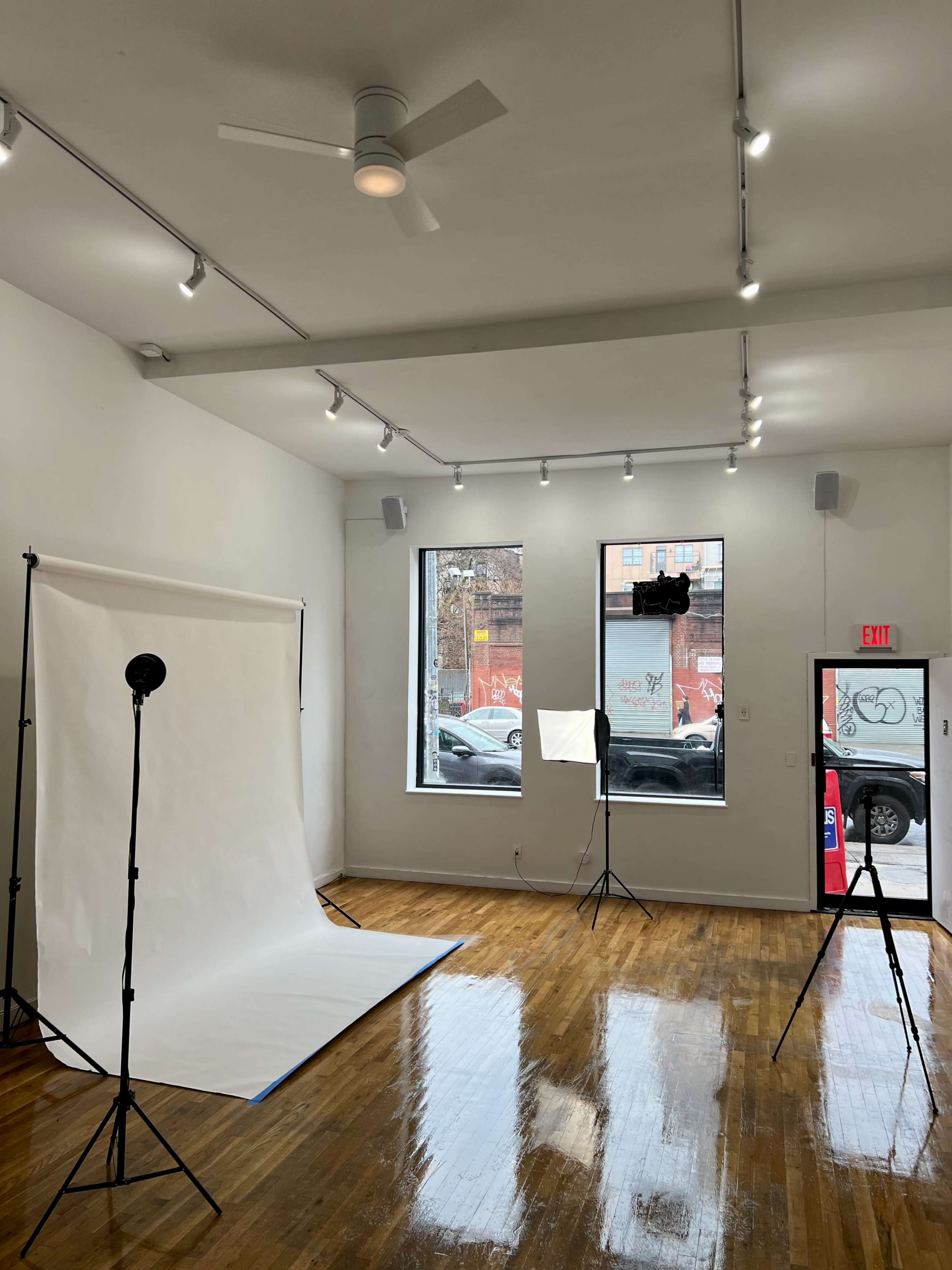A bright photography studio with a backdrop, lighting equipment, and large windows.