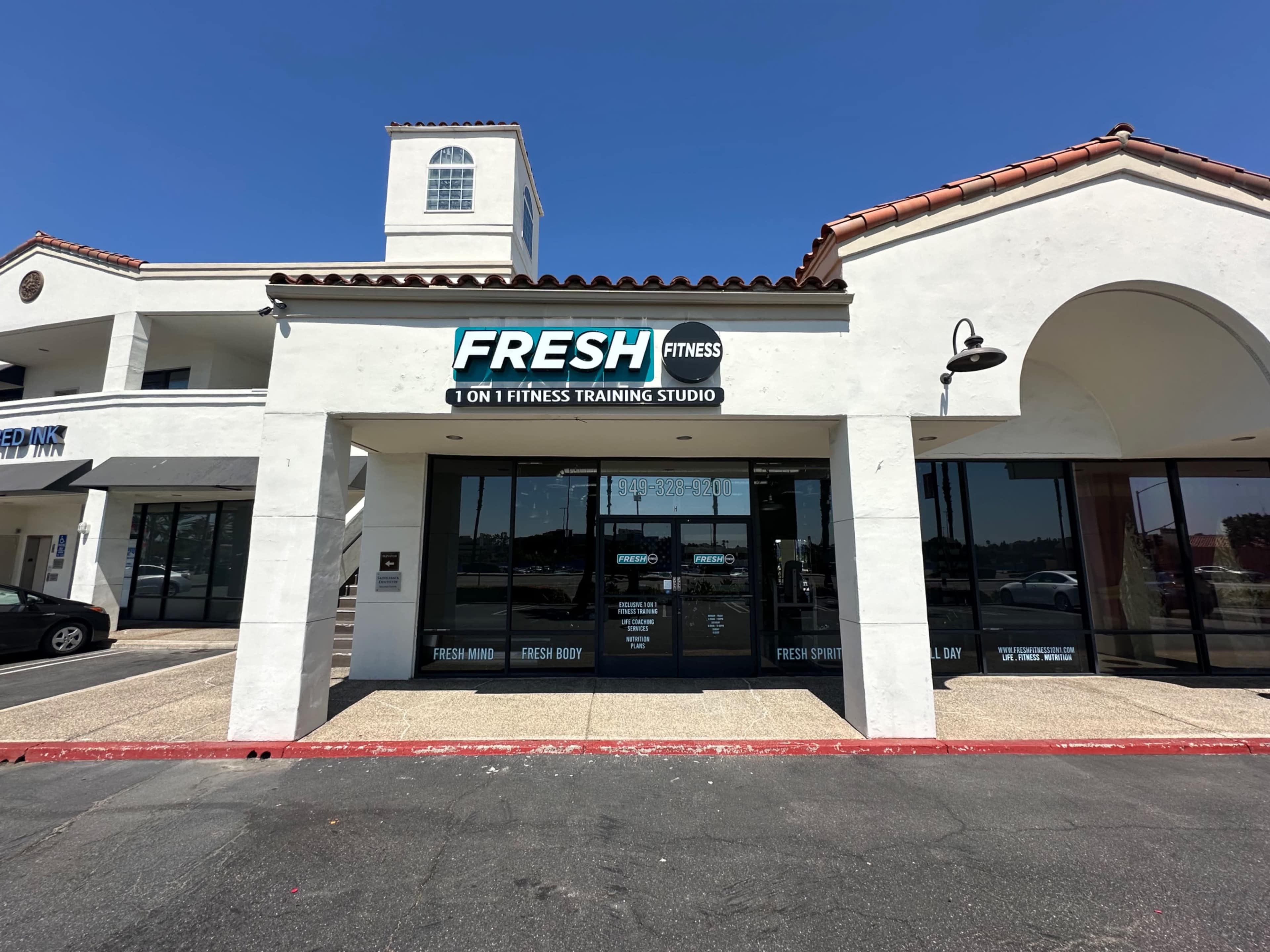 The image shows a fitness training studio named "FRESH FITNESS," located in a commercial building with a white exterior and a red pavement in front.