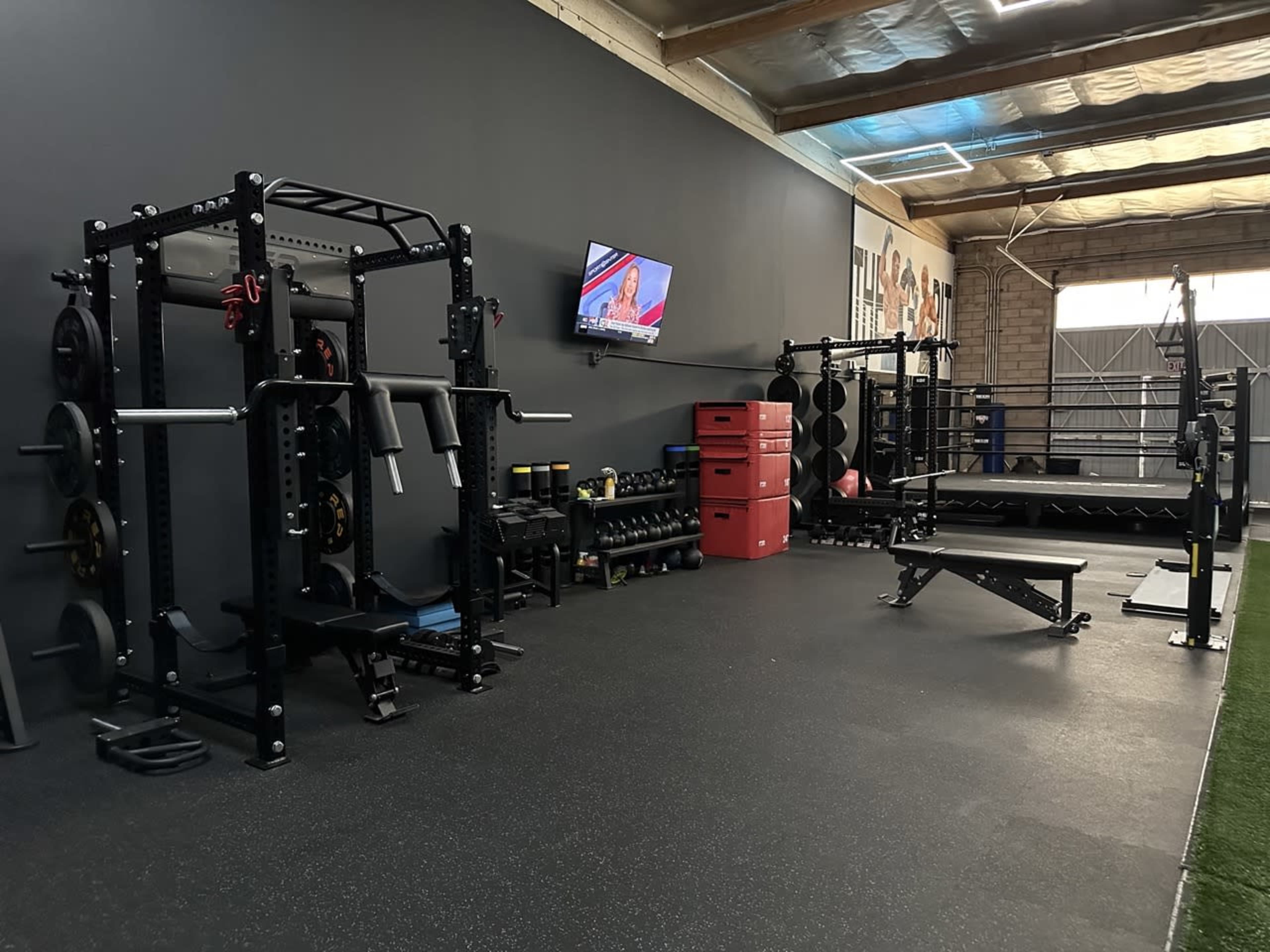 A well-equipped gym space featuring weightlifting equipment, benches, and a television mounted on the wall.