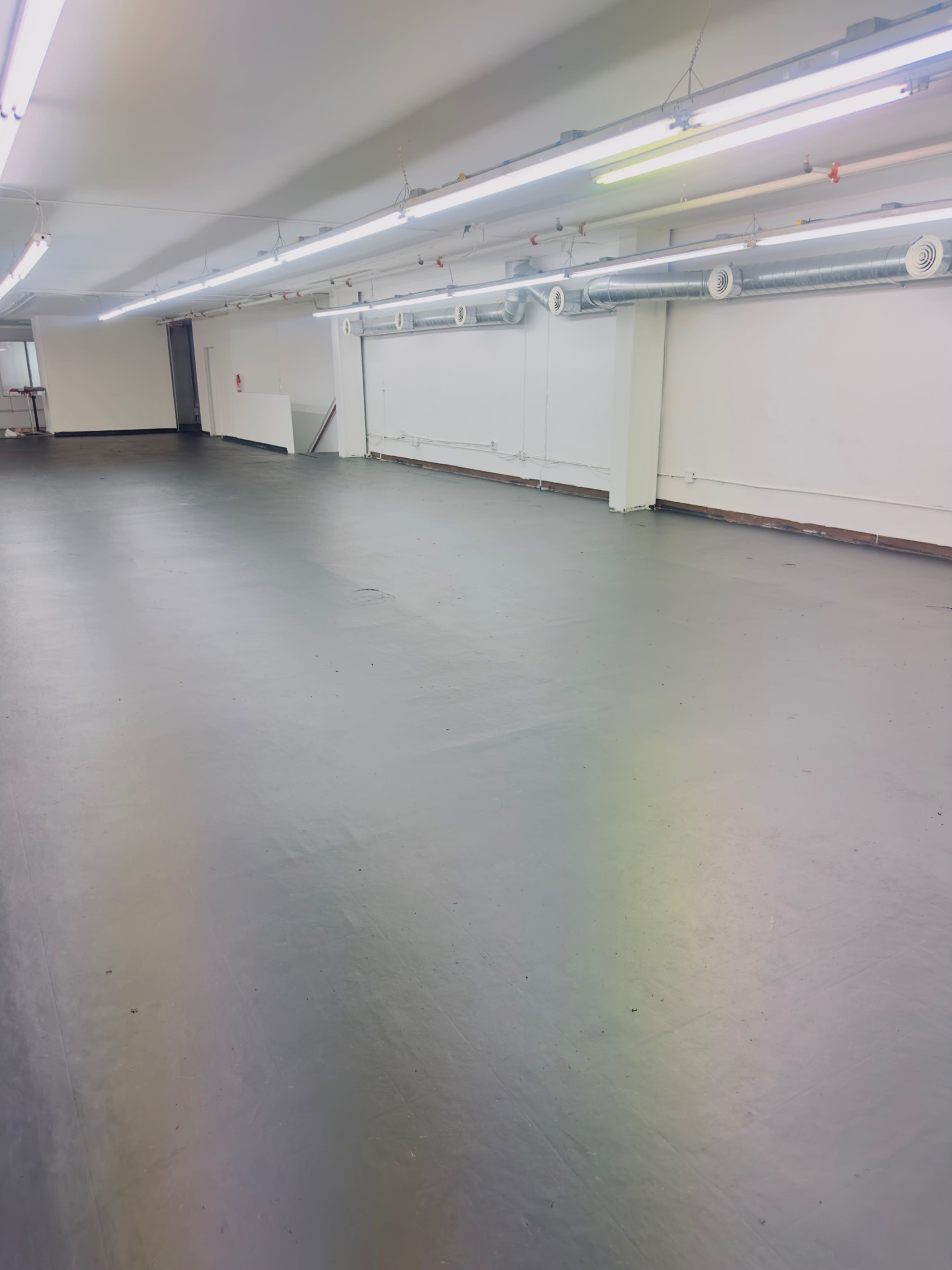 The image shows a spacious, empty indoor area with polished gray flooring and fluorescent lighting along the ceiling.