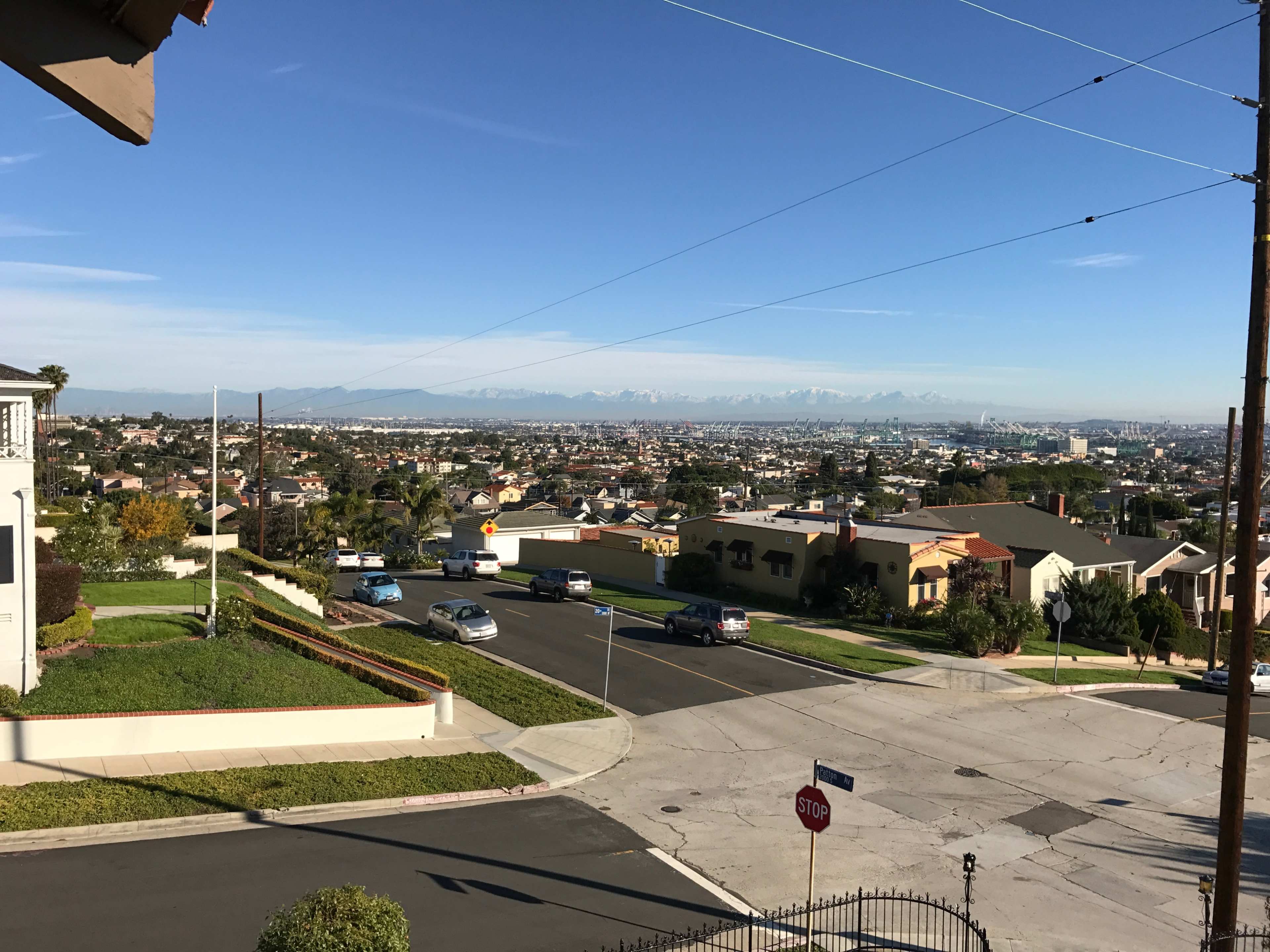 A view from a hillside showing a residential area with houses, streets, and distant mountains under a clear blue sky.