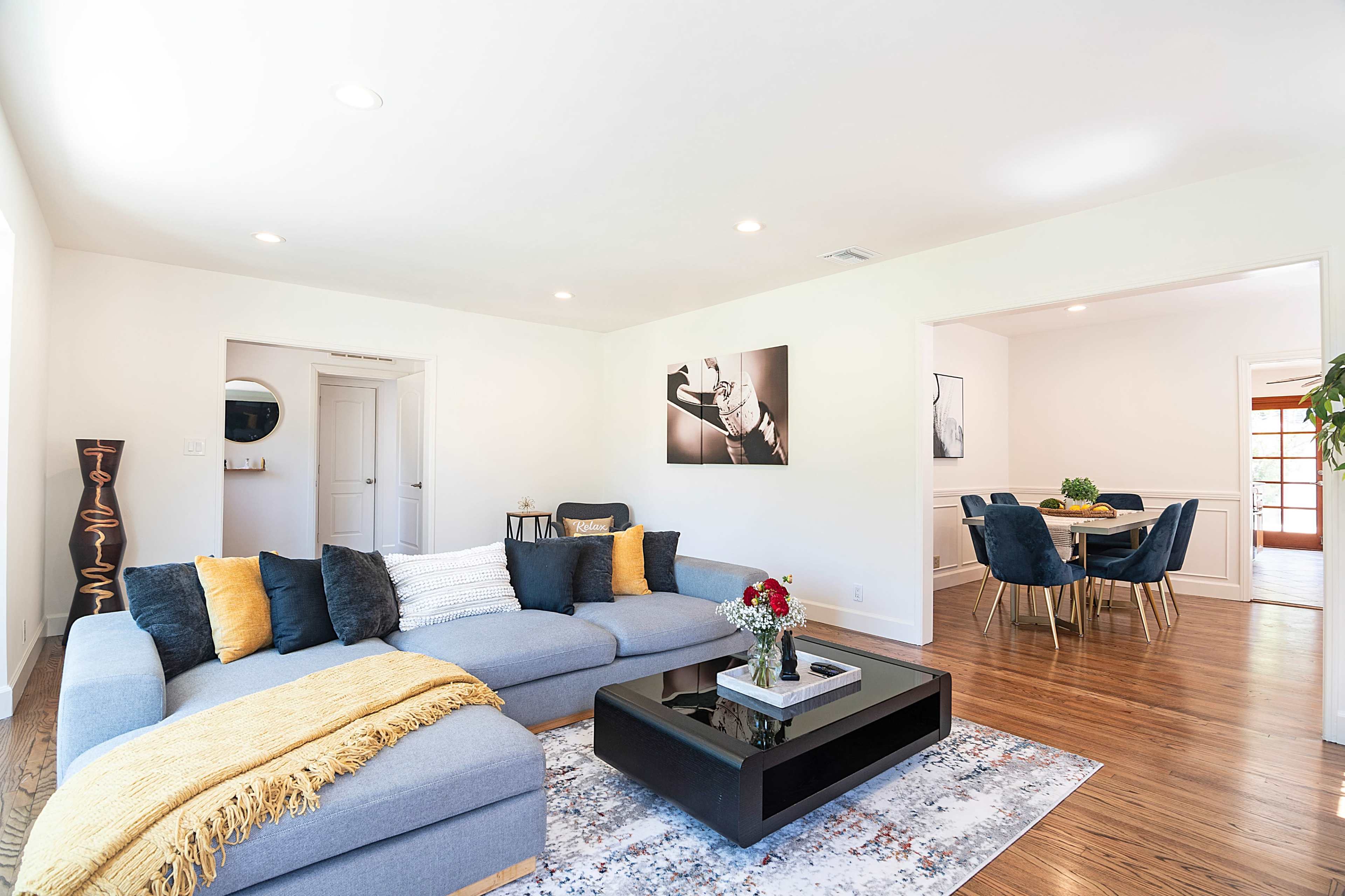 The image shows a modern living room featuring a large sectional sofa, a coffee table, and an adjacent dining area with a round table and chairs.