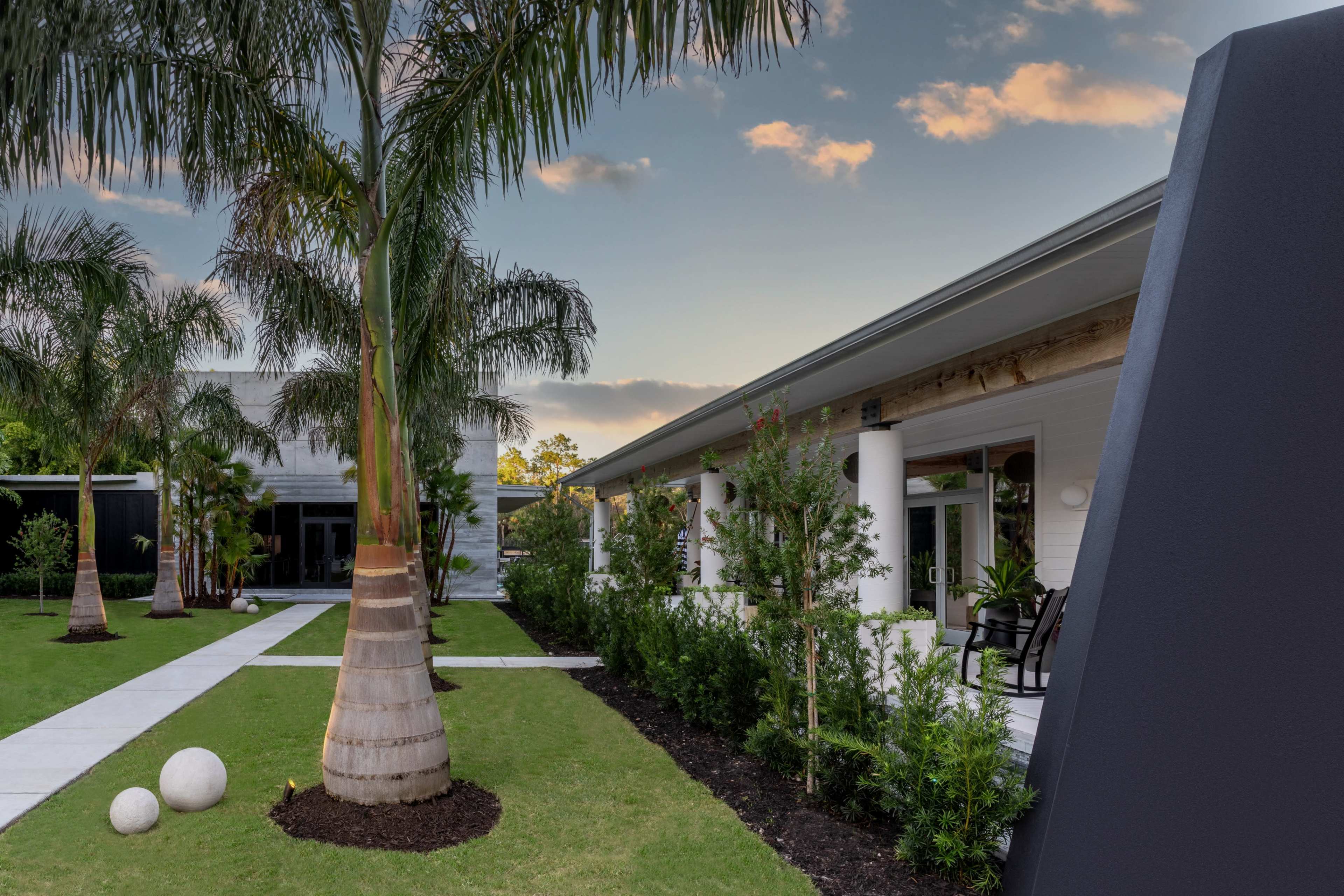 A landscaped outdoor area with palm trees, a grassy lawn, and modern buildings in the background.