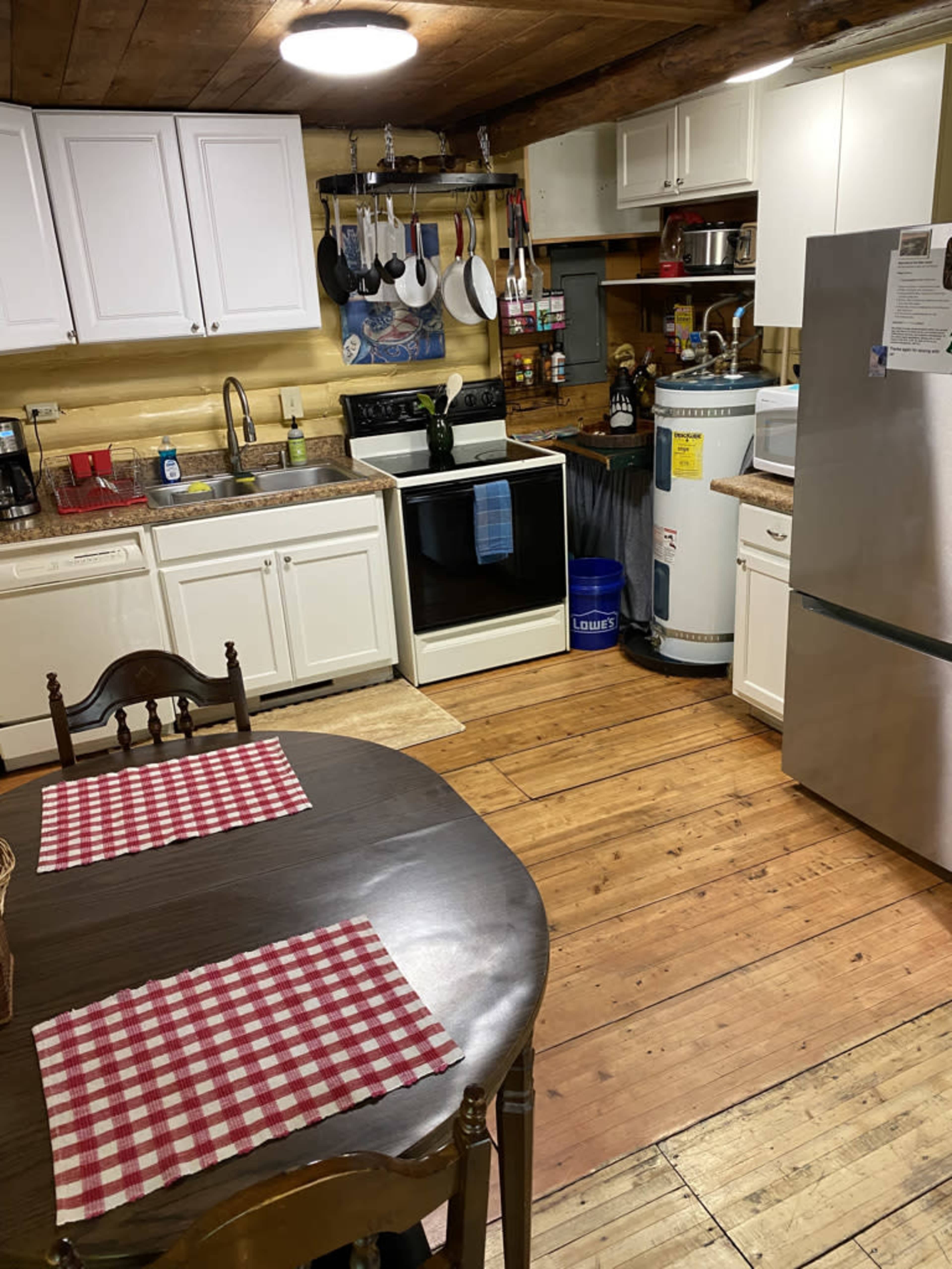 A kitchen with white cabinets, a black stove, a stainless steel refrigerator, and a wooden table set with checkered placemats.