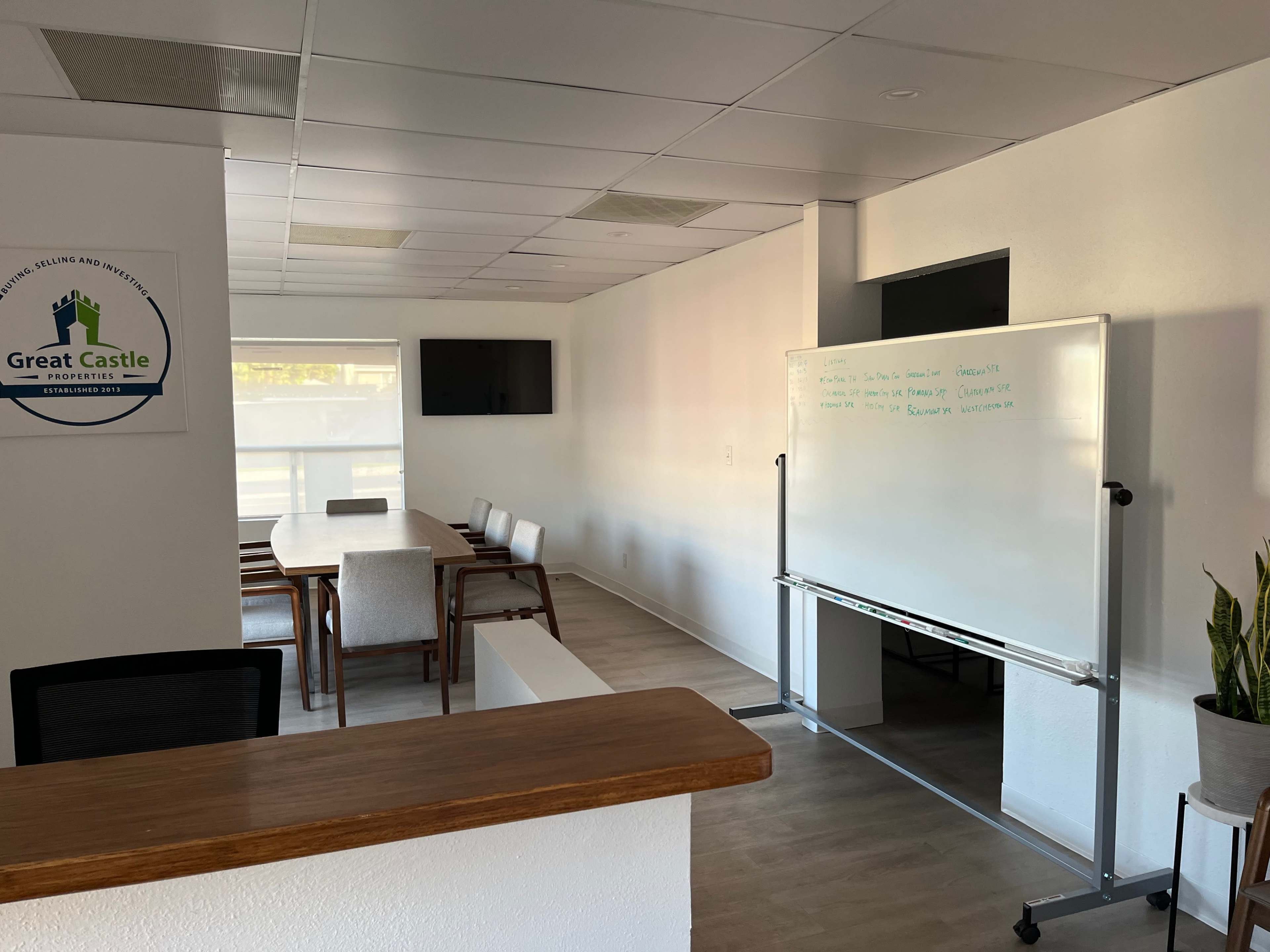 A modern office space with a conference table, whiteboard, and a large screen on the wall.