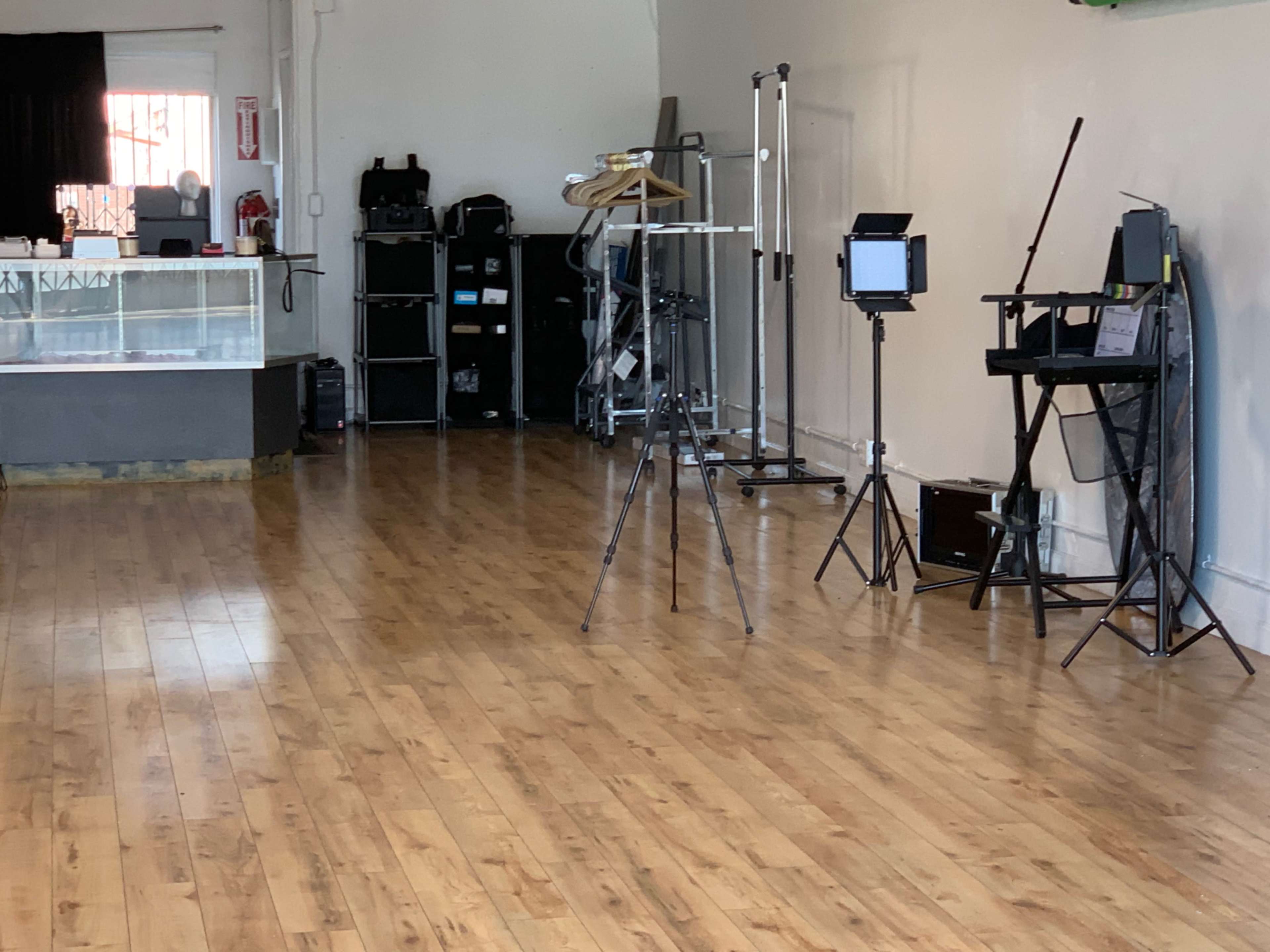 A spacious room with wooden flooring, featuring equipment like tripods, a folding chair, and various storage units against the walls.