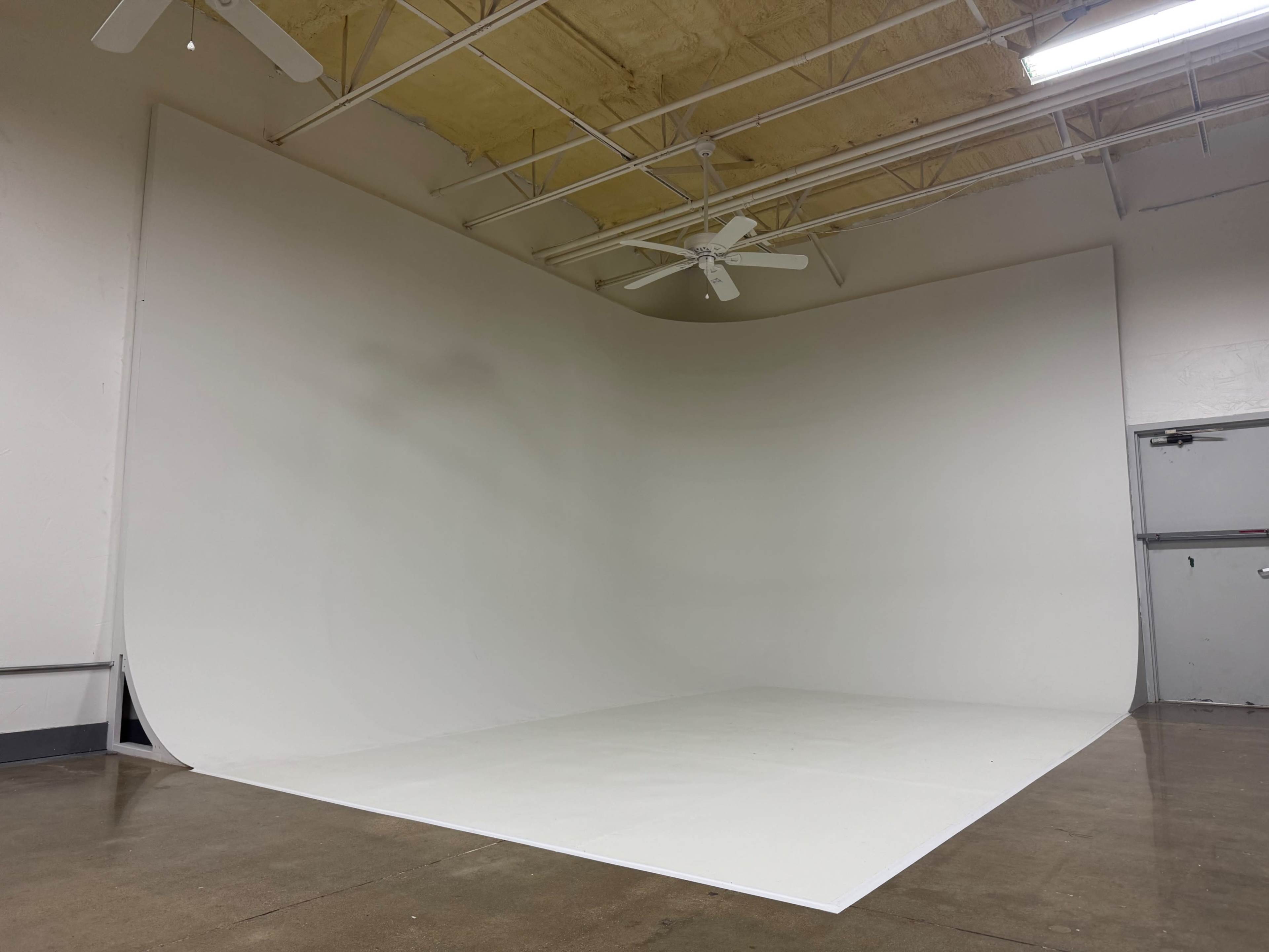 The image shows a large, blank photography backdrop in a spacious room with a polished concrete floor and ceiling fans.