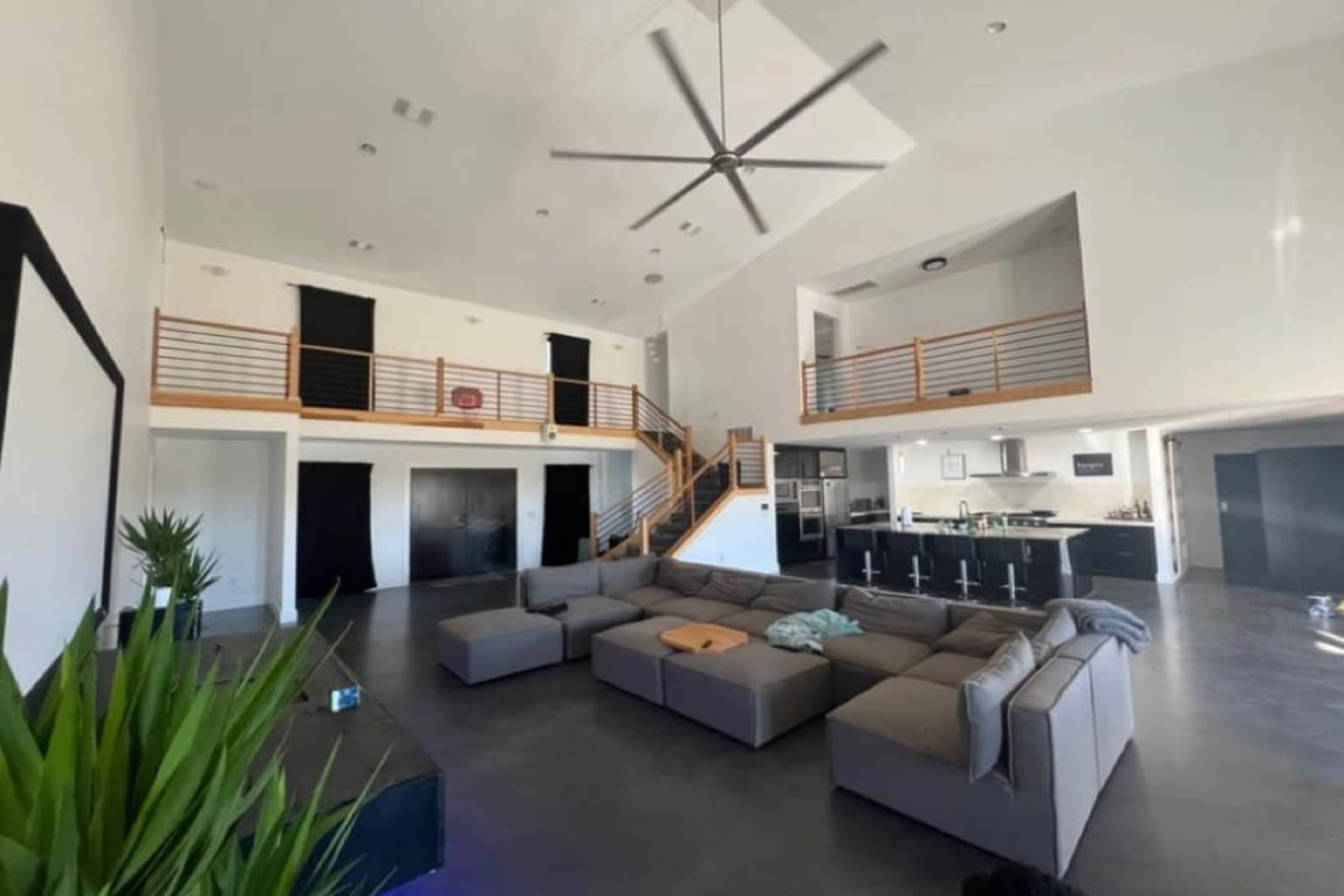 A spacious living room with a large sectional sofa, a balcony overlooking the main area, and a modern kitchen in the background.