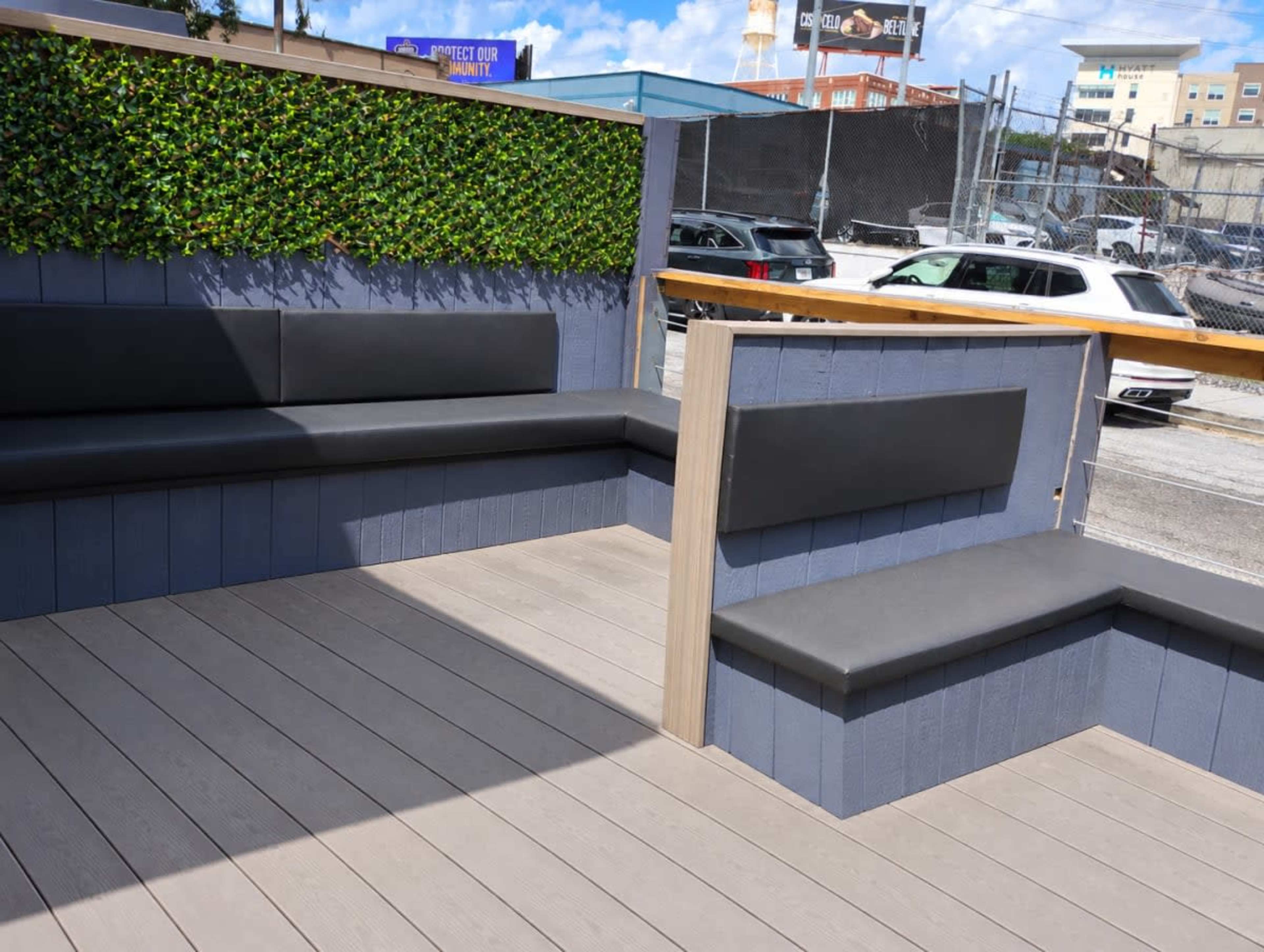 The image shows a modern outdoor seating area with black benches and a green wall of plants in a partially enclosed space.