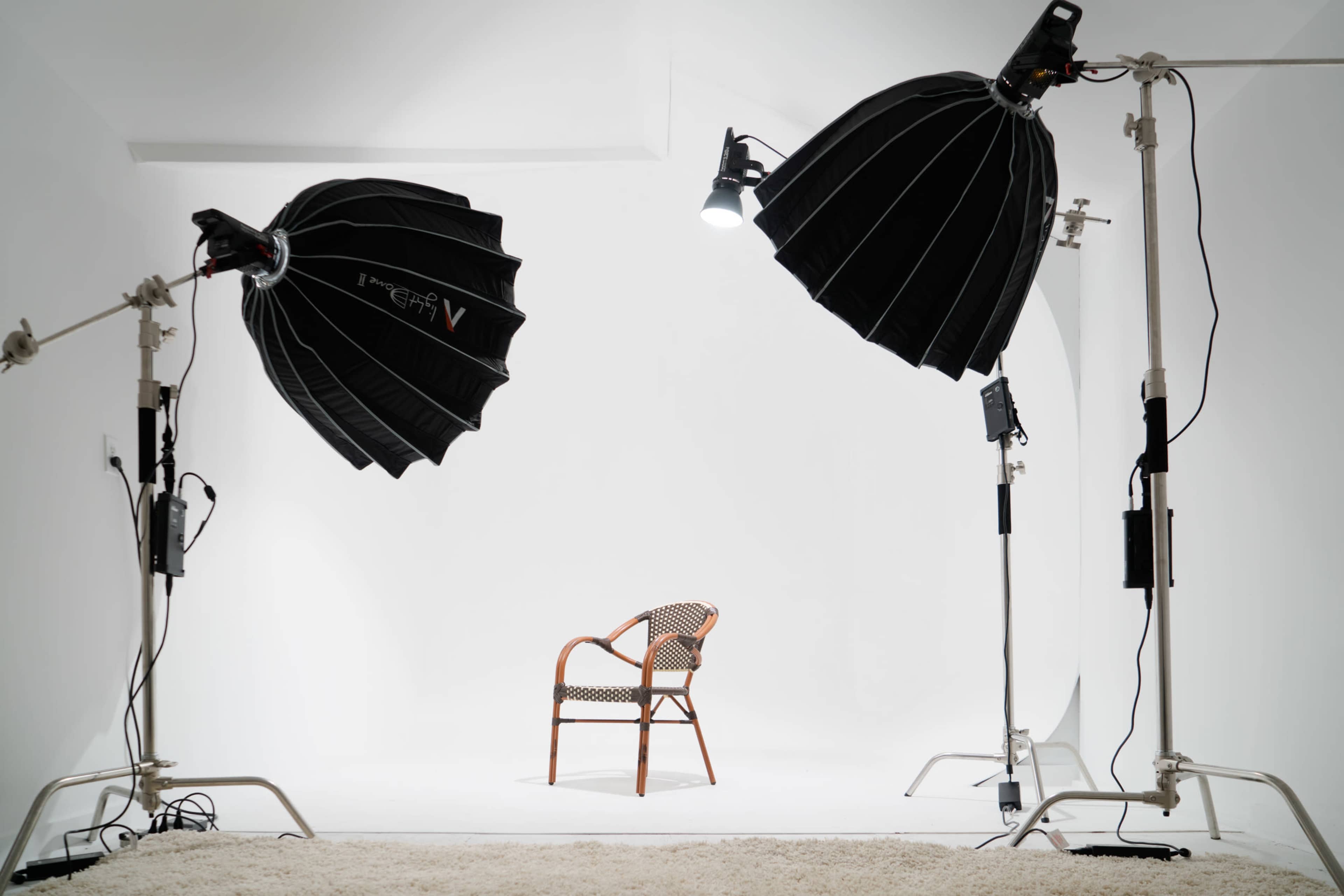 A photography studio is set up with two softbox lights illuminating an empty chair on a white backdrop.