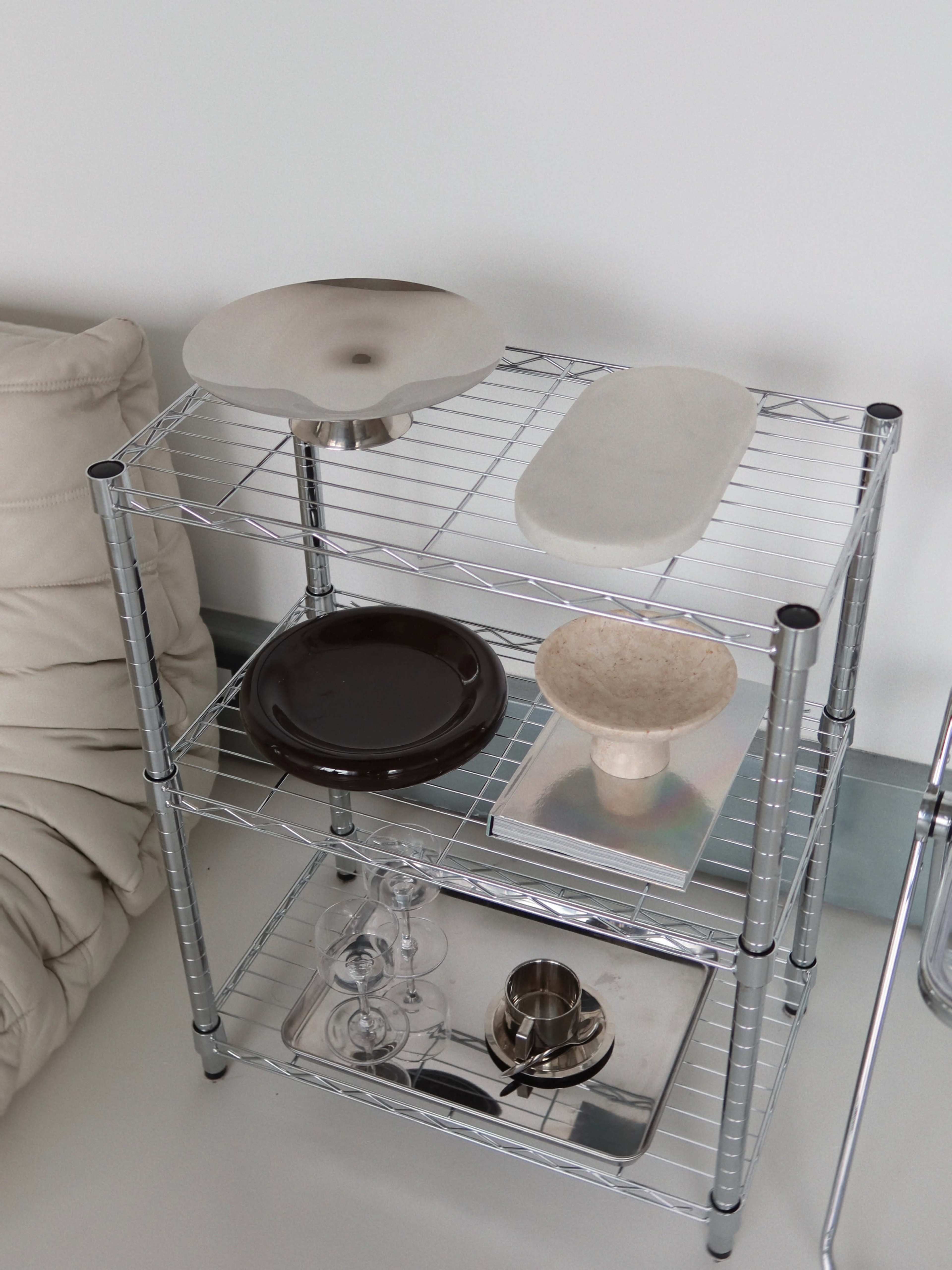 A metal shelving unit holds various ceramic dishes and glassware in a minimalist setting.