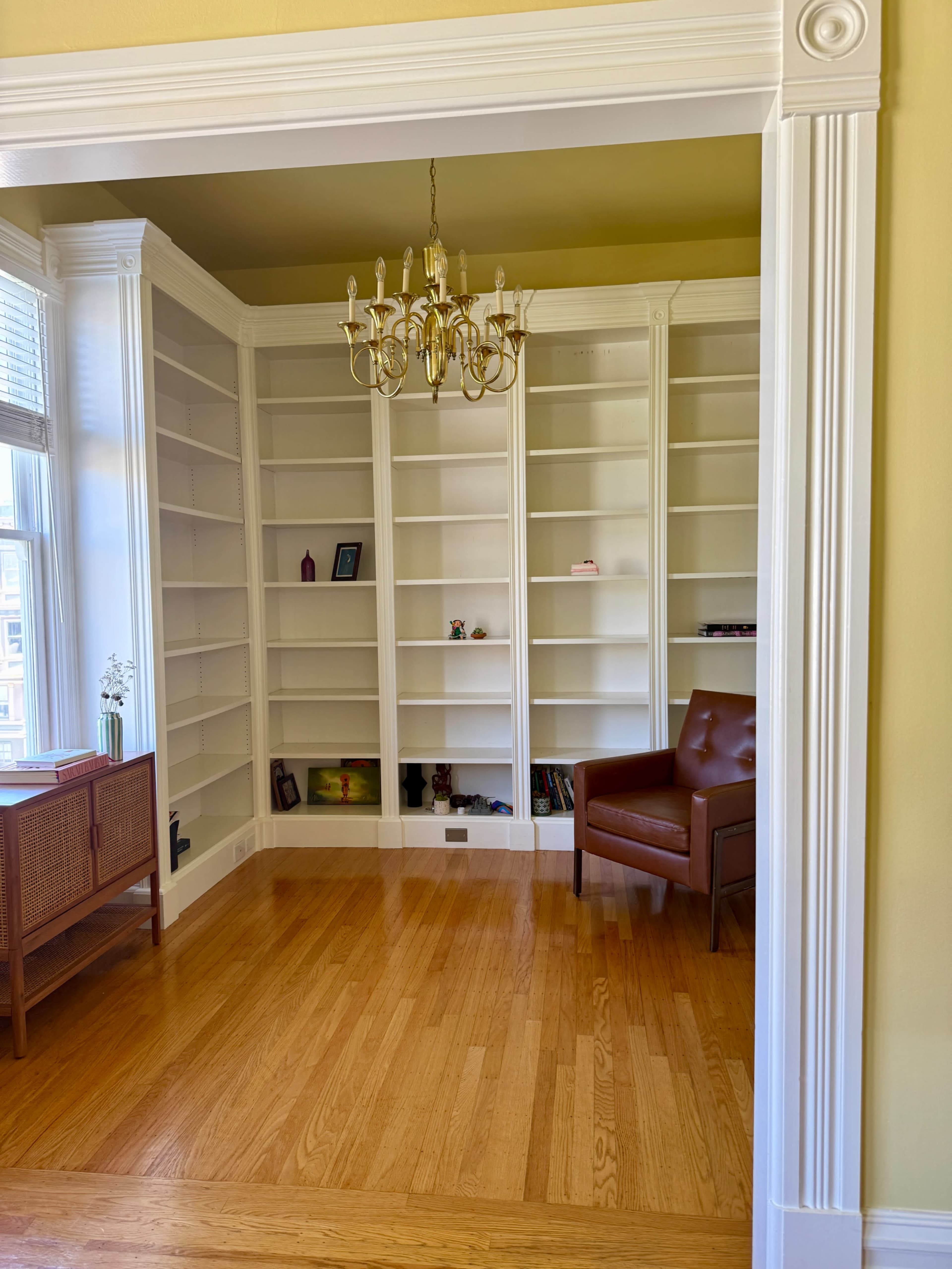 The image shows a bright room with white bookshelves, a brown leather chair, and hardwood flooring.