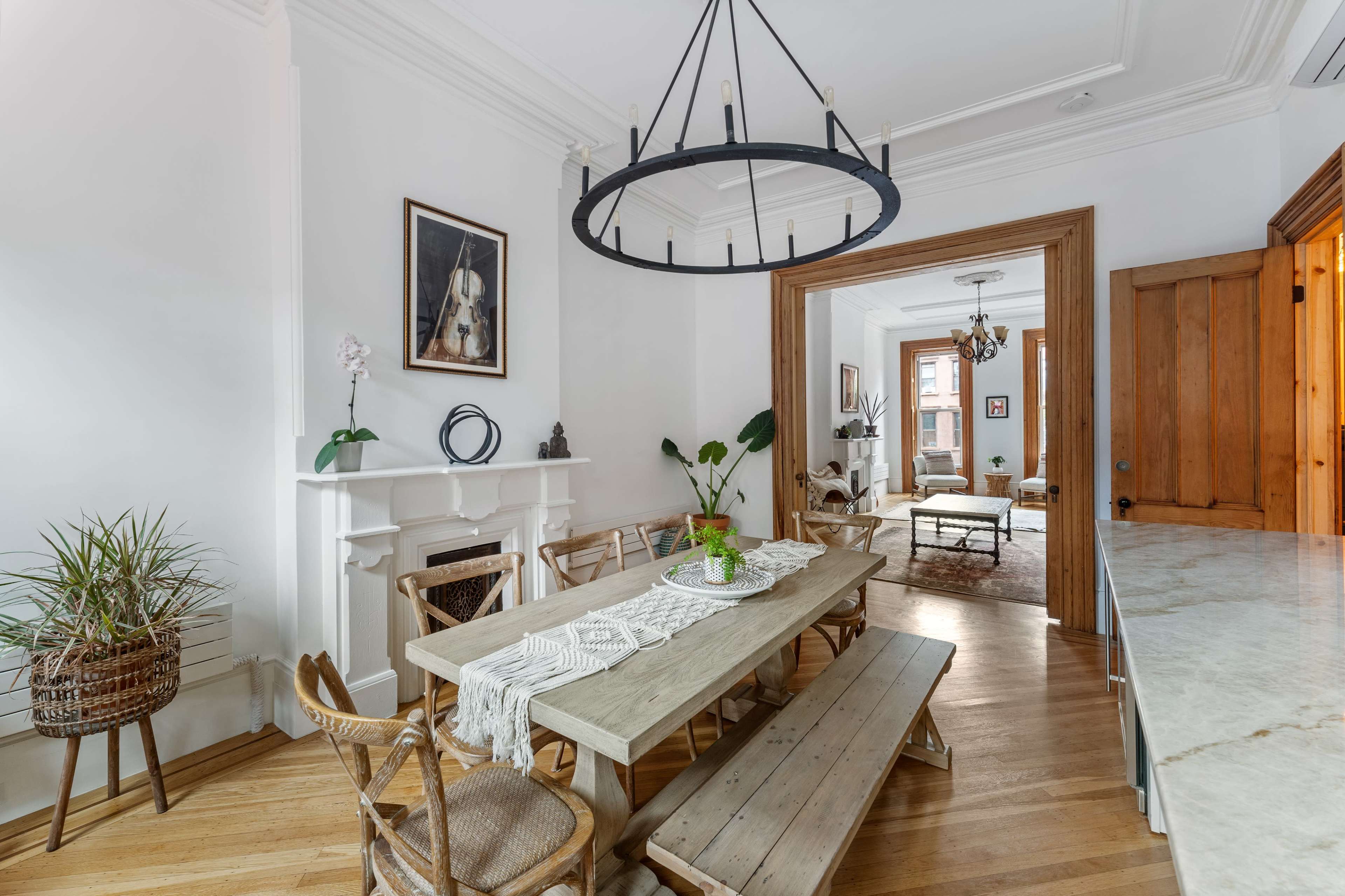 A dining area features a large wooden table surrounded by chairs, with a chandelier overhead and a doorway leading to a living space.