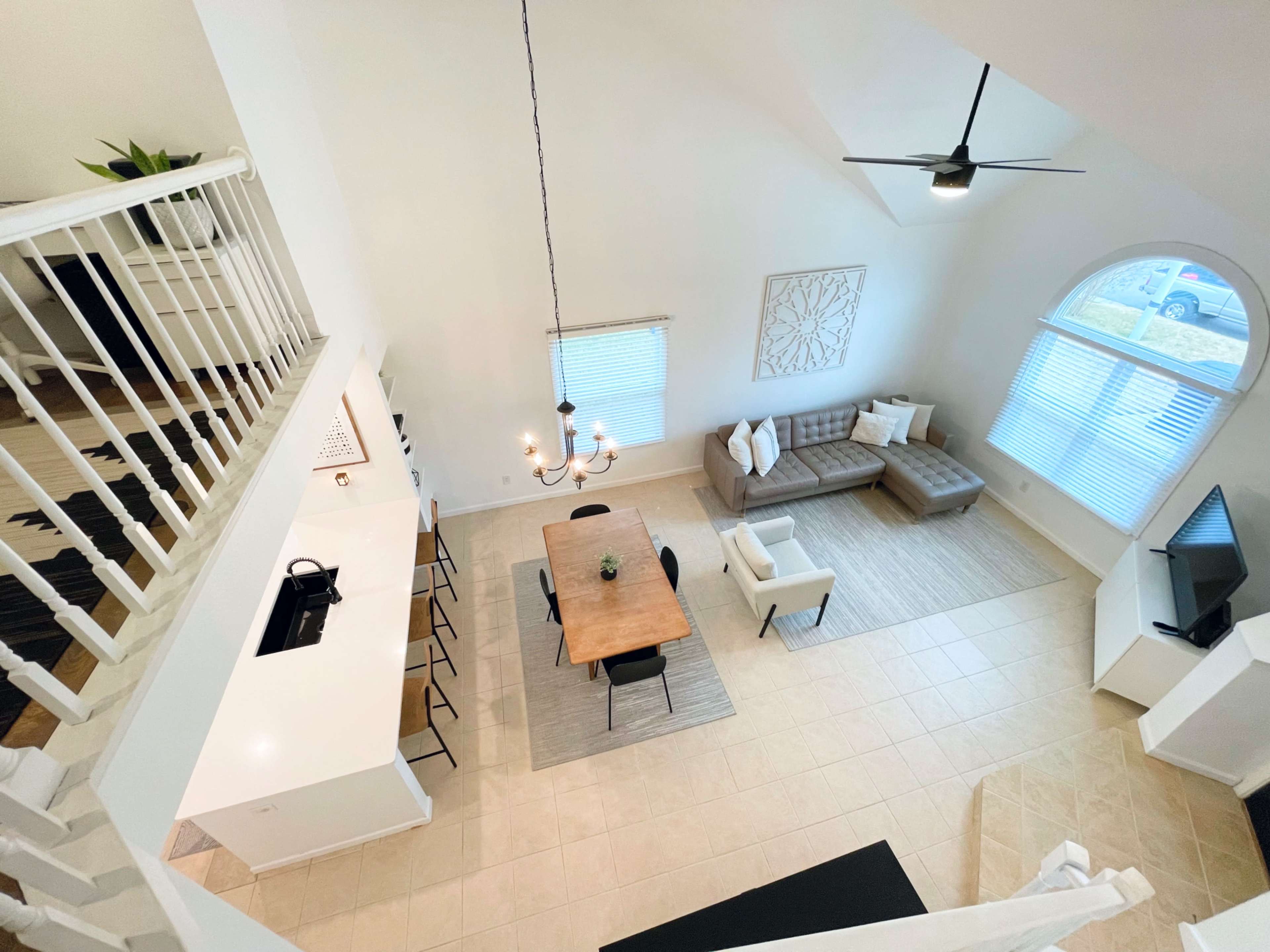 The image shows an open-concept living area with a dining table, a sectional sofa, and a kitchen visible from a high angle.