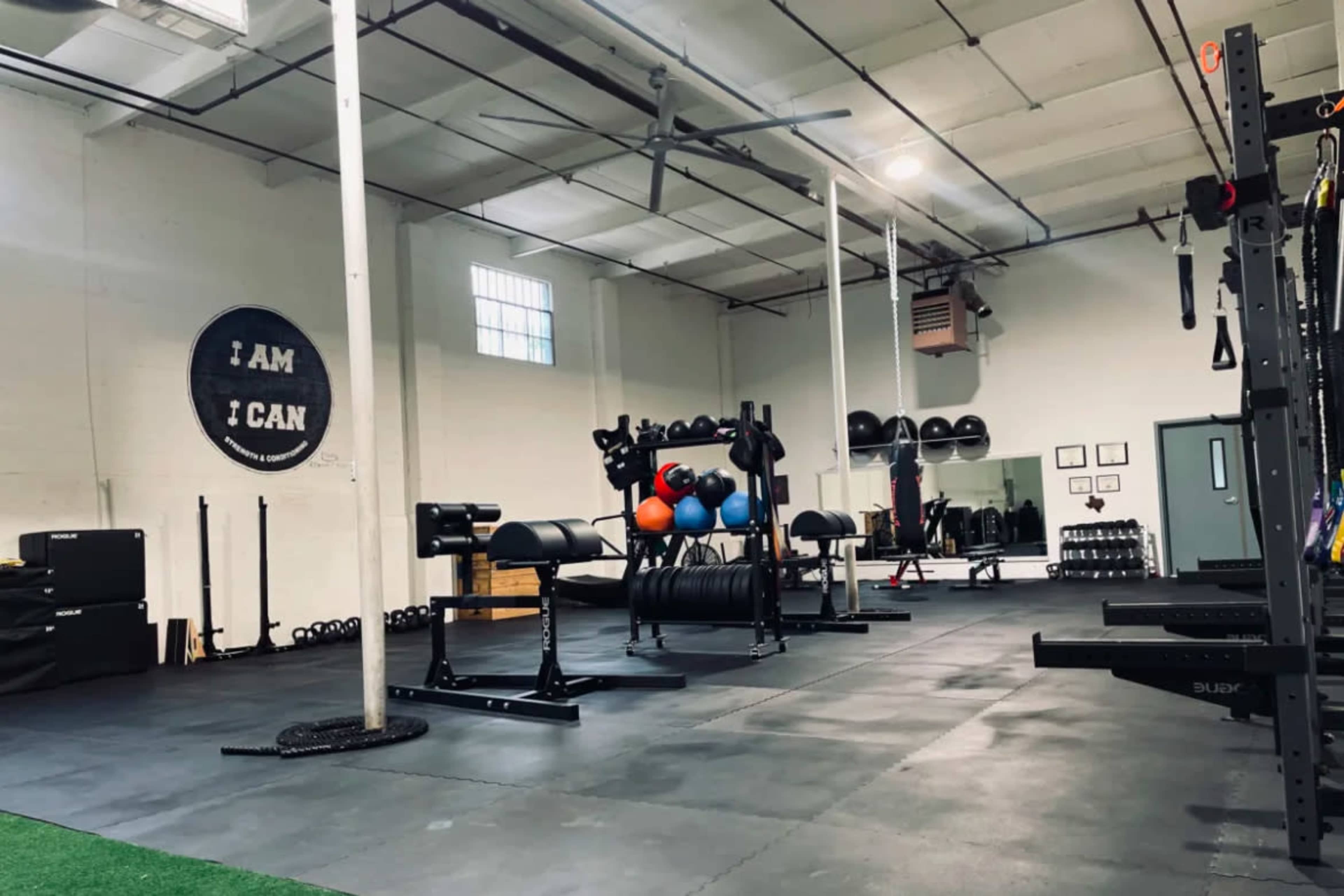 A spacious gym with various weightlifting equipment, exercise balls, and a motivational wall mural.