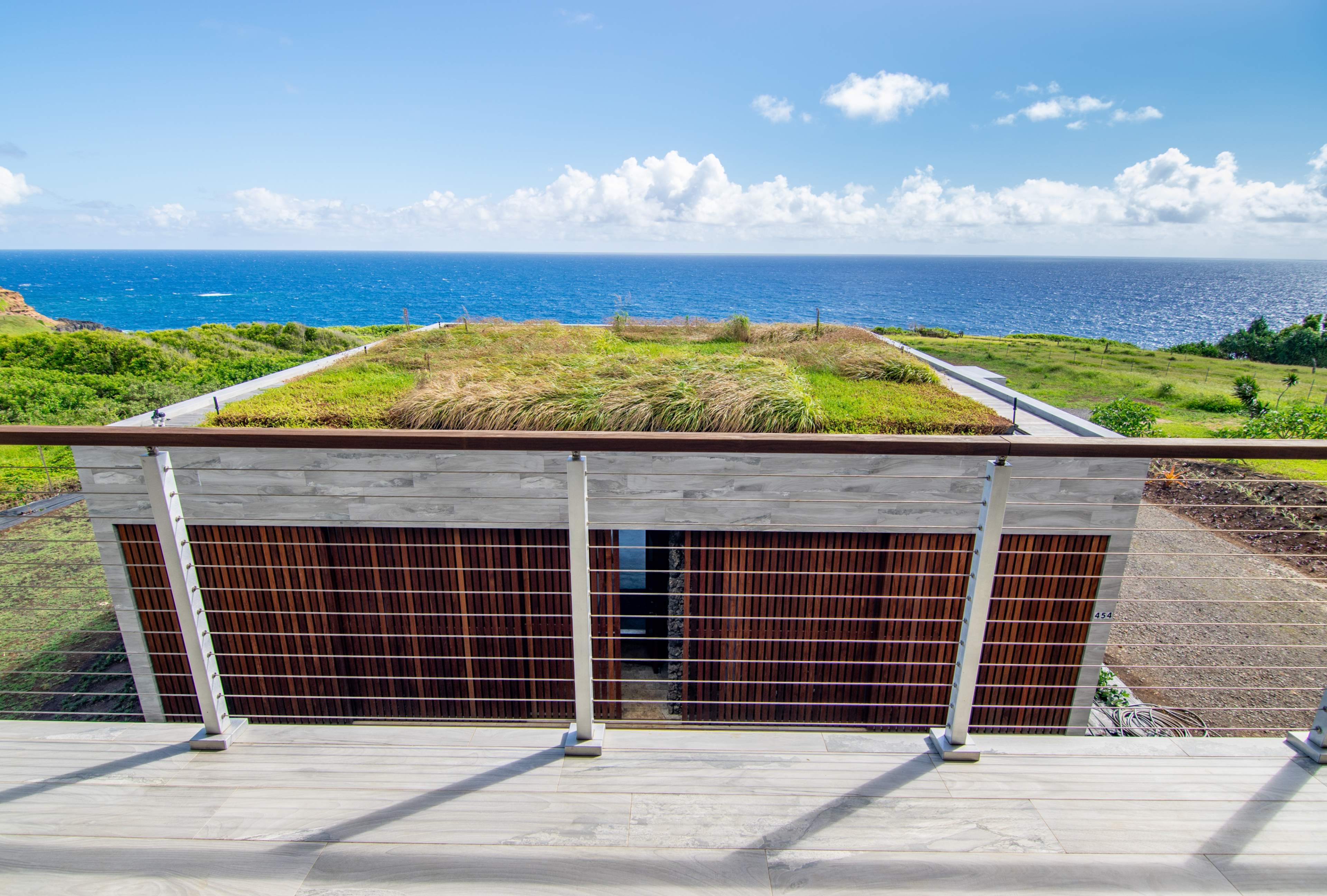 A modern building with a grass-covered roof overlooks a lush landscape and the ocean.
