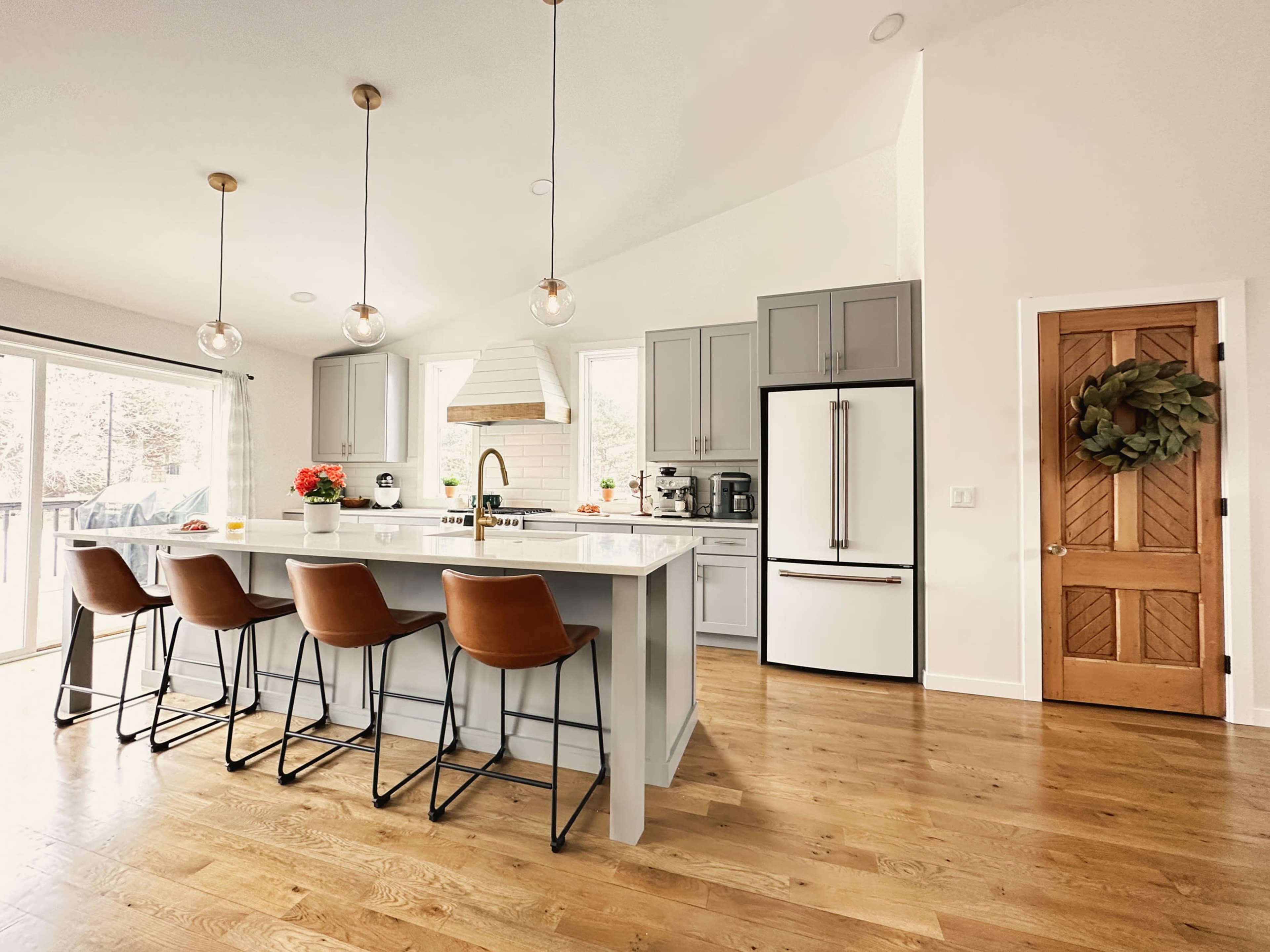 The kitchen features a large island with four bar stools, modern cabinetry, a refrigerator, and natural light from sliding glass doors.