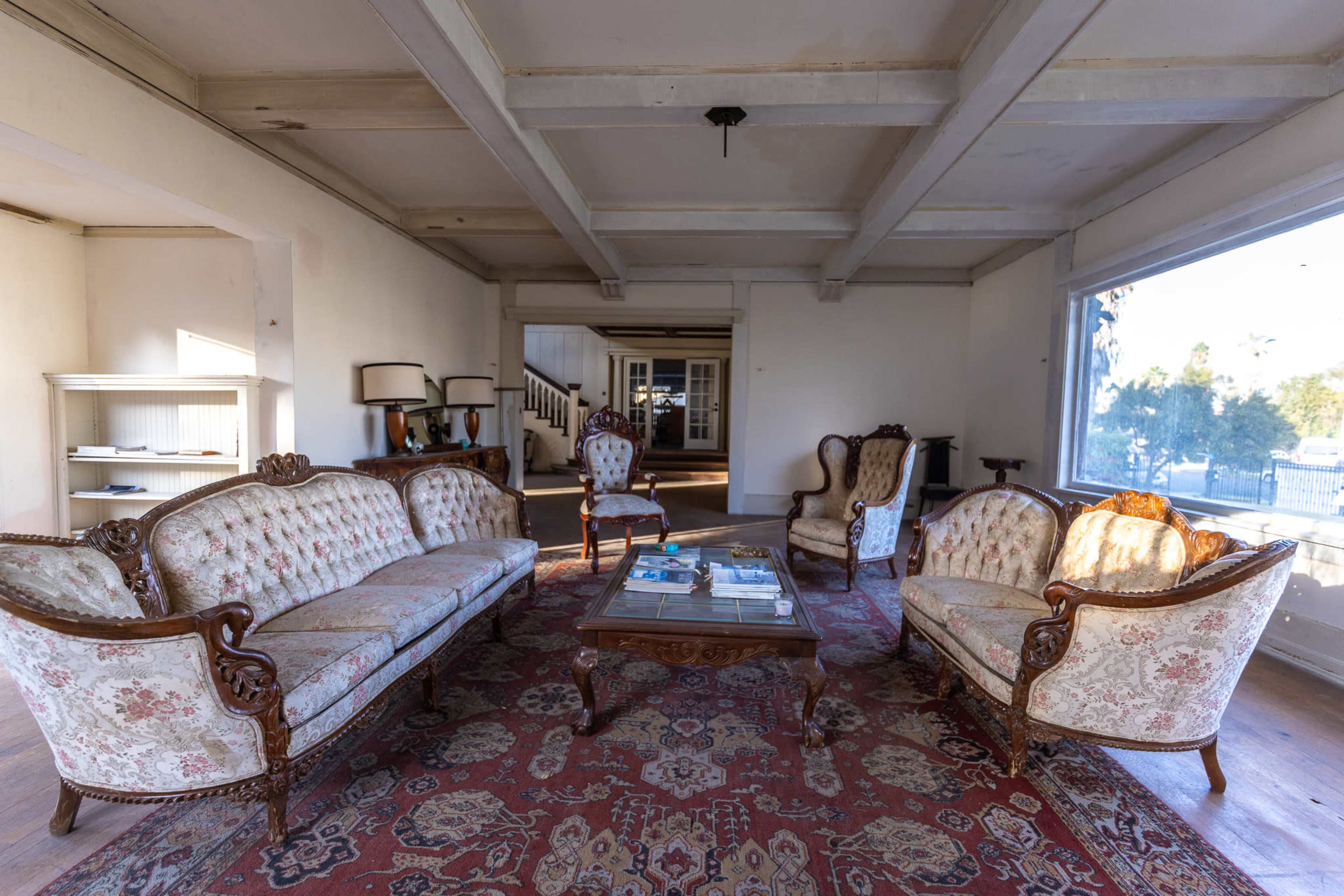 The room features ornate wooden furniture with floral upholstery arranged around a coffee table on a patterned rug.