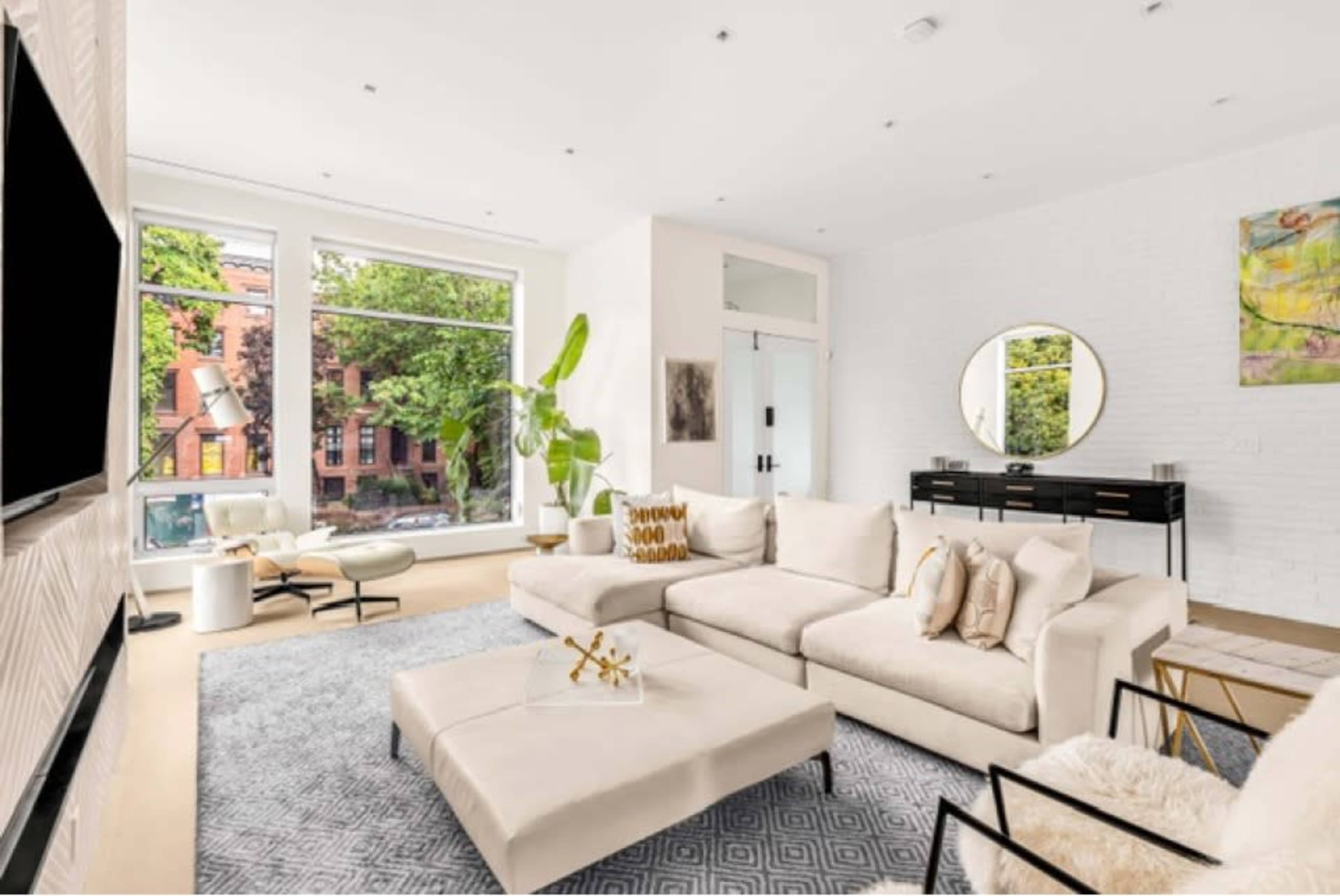 A modern living room featuring a large sectional sofa, a coffee table, and windows with views of trees outside.
