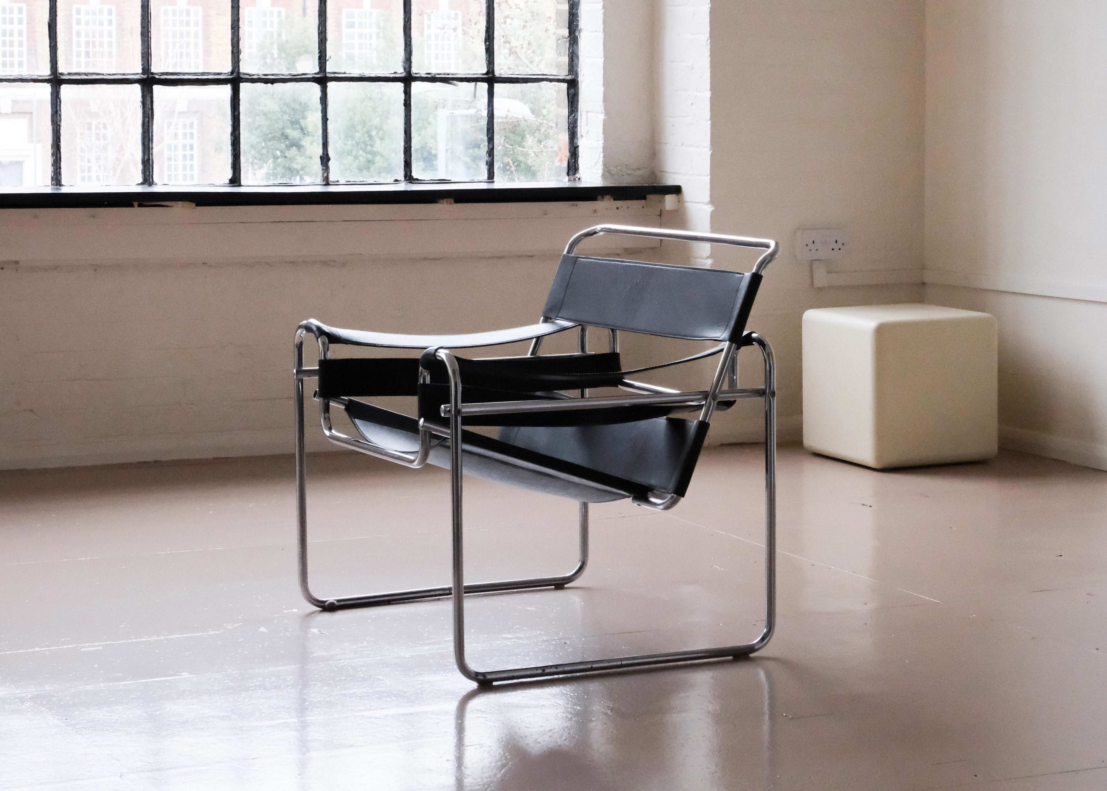A black and chrome lounge chair is positioned alone in a spacious, well-lit room with large windows.