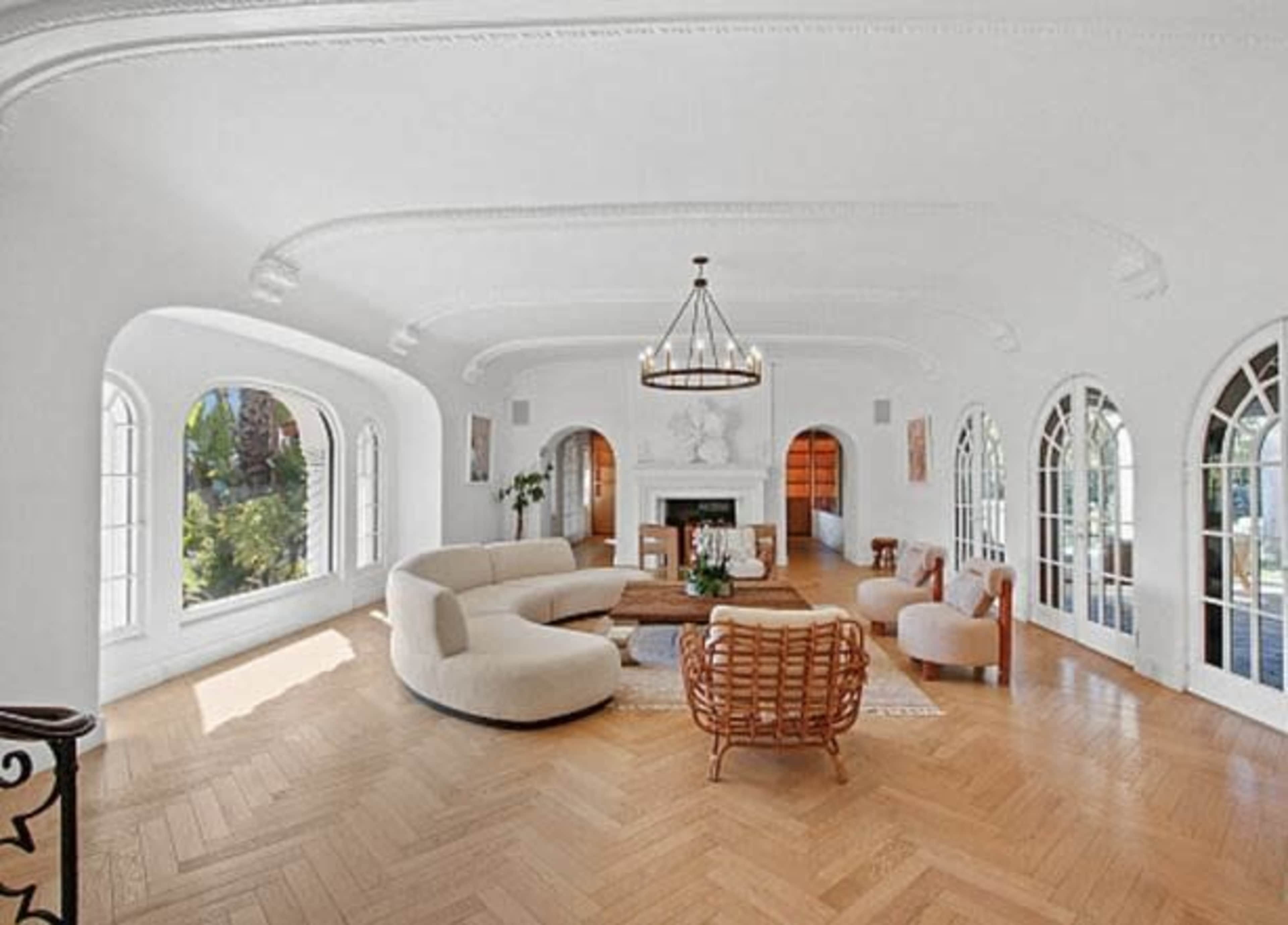 The spacious living room features large arched windows, a curved beige sofa, a wooden coffee table, and elegant hardwood flooring.
